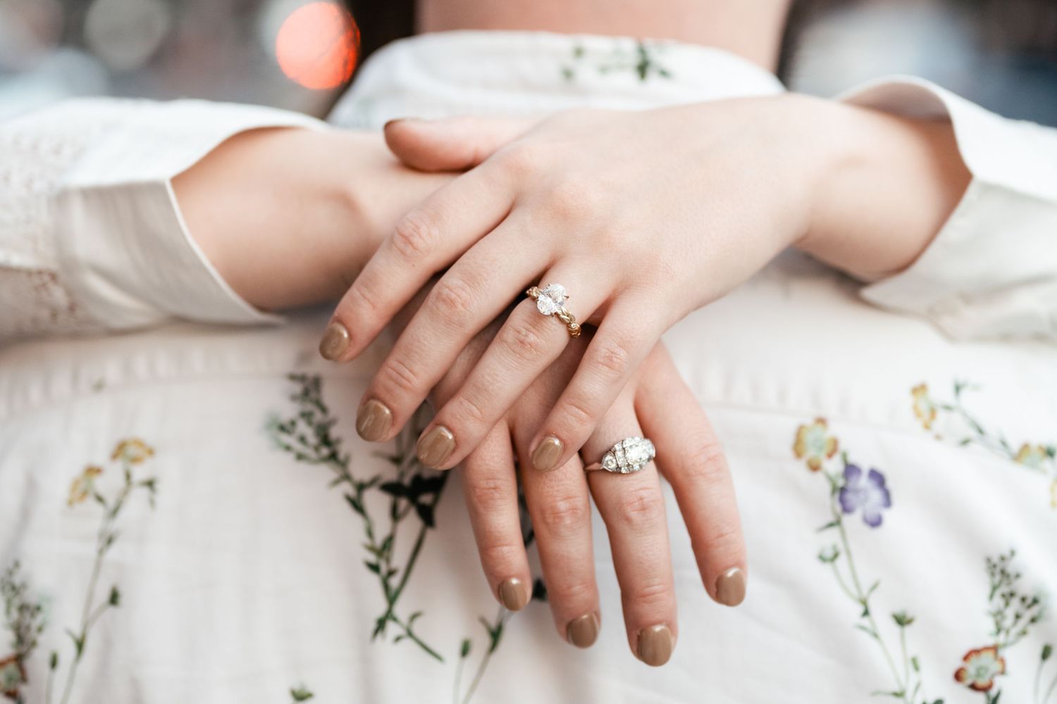 Close-up of hands resting on delicate white lace with scattered small flowers and pearls in a bridal setting. Engagement Photographer.