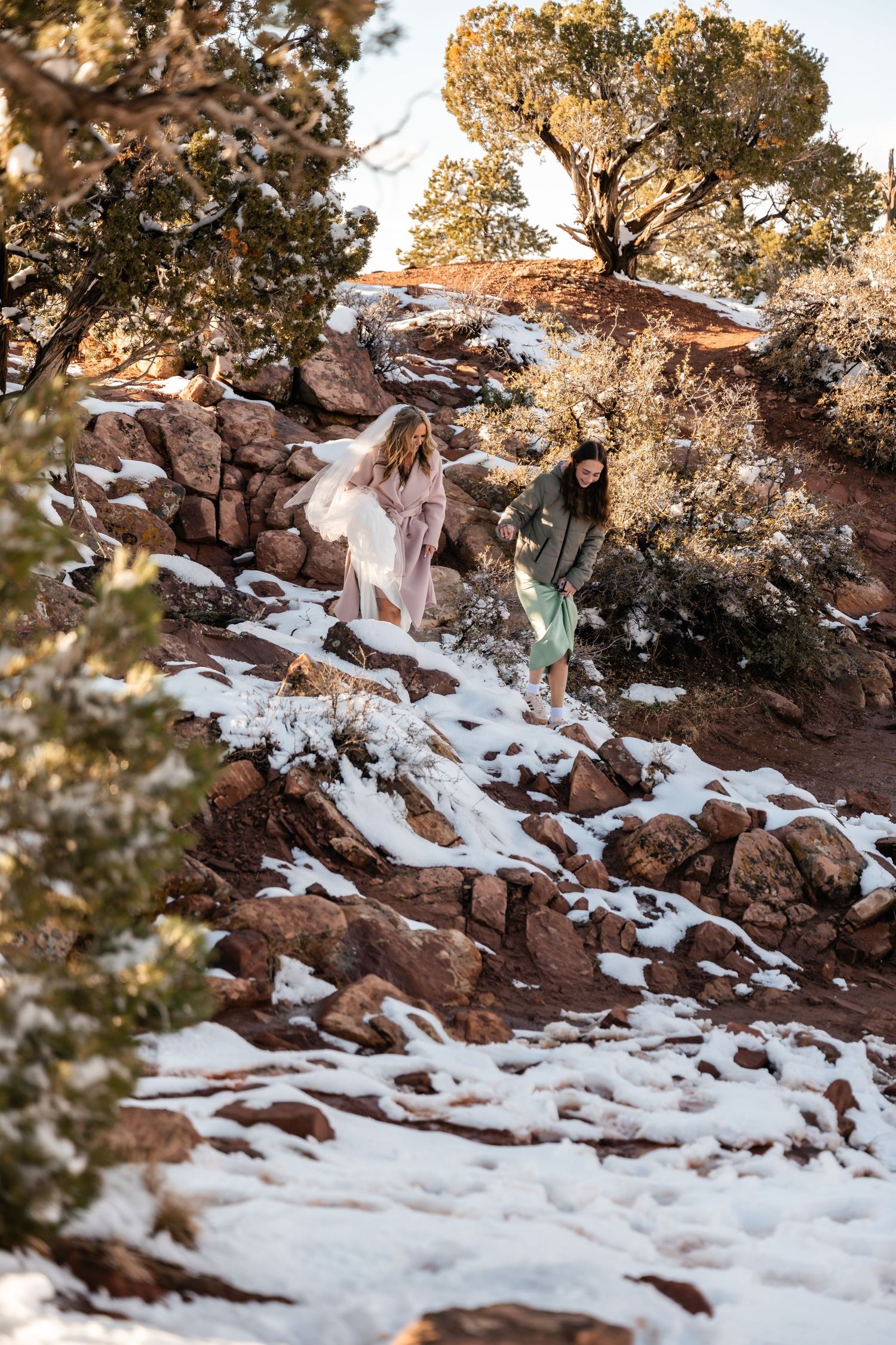 Snow covered red rock trail winding through desert landscape with scattered juniper trees.