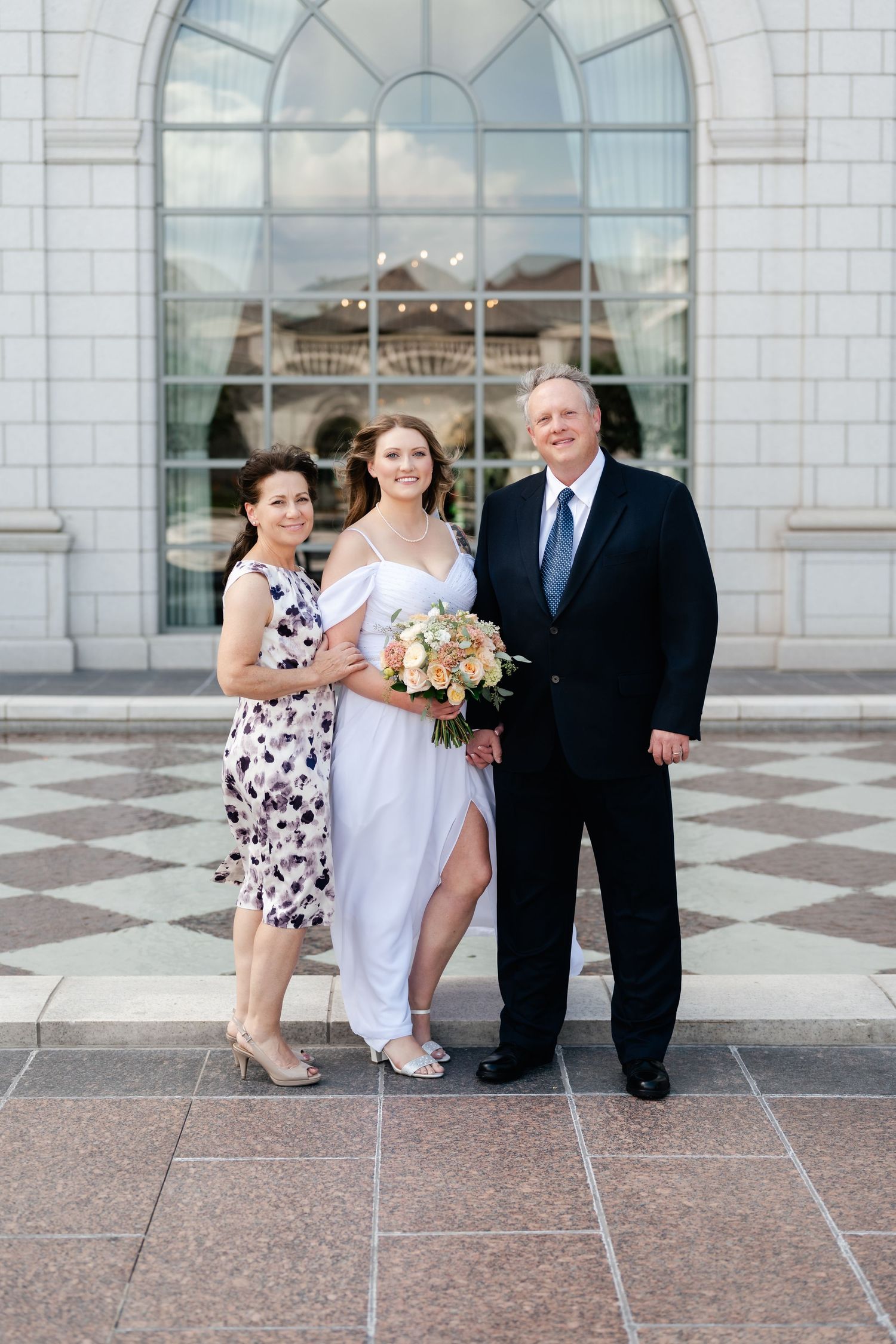 Group gathers for formal photos outside a Mormon temple with elegant architecture and arched windows.