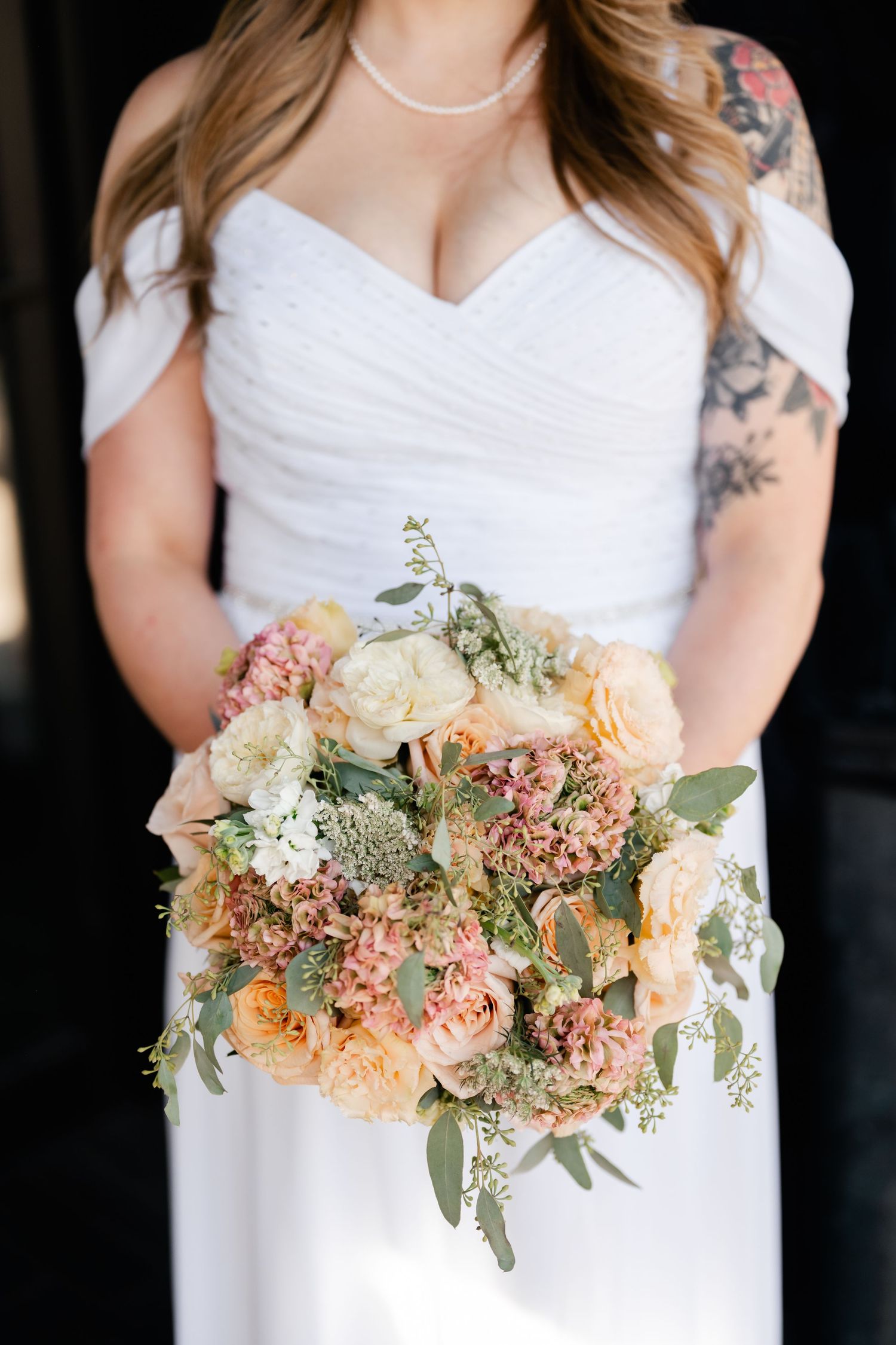 Bridal bouquet featuring peach and pink flowers with eucalyptus leaves against white dress.