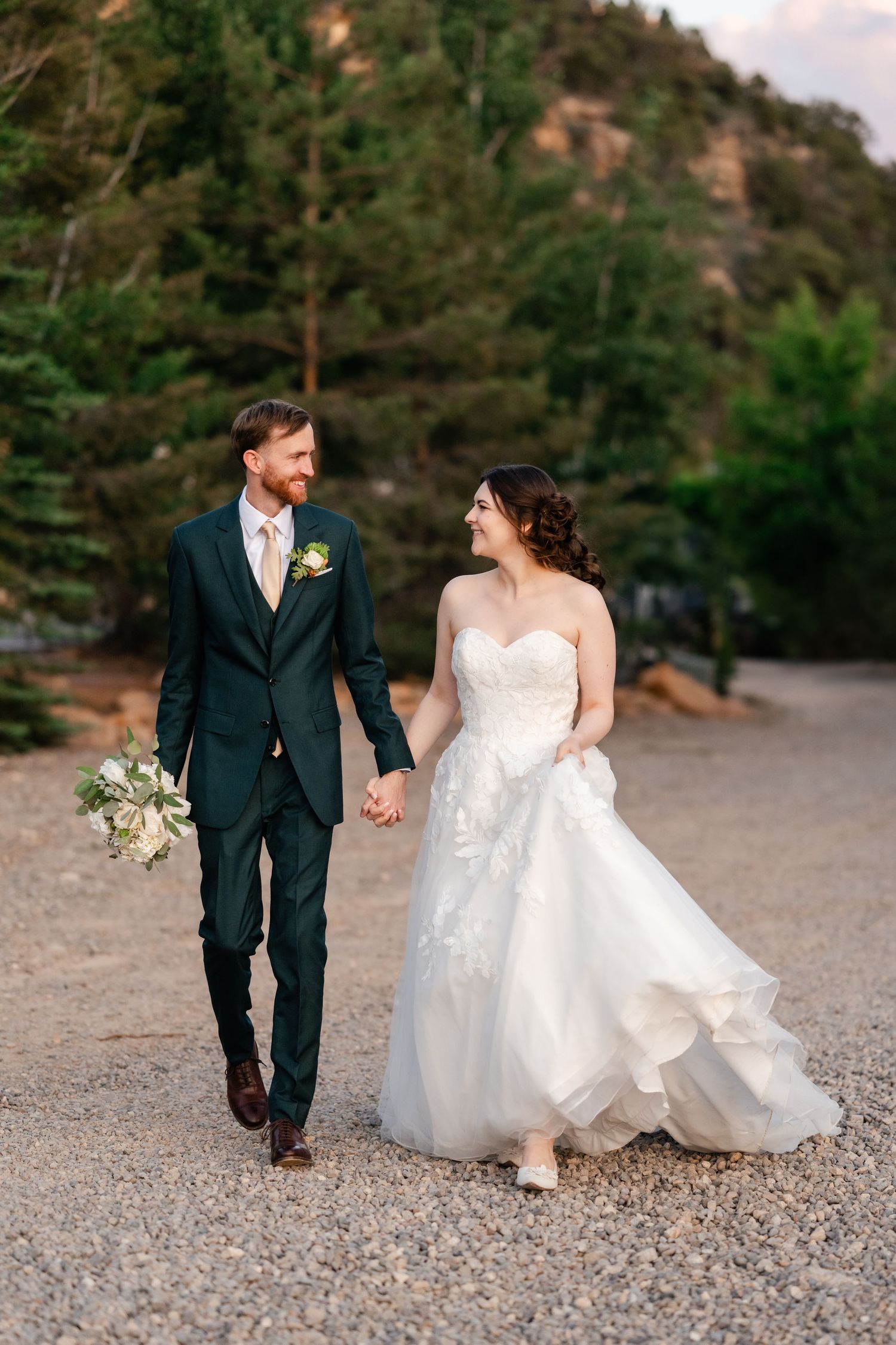 Wedding couple walks hand in hand on a rocky mountain path.