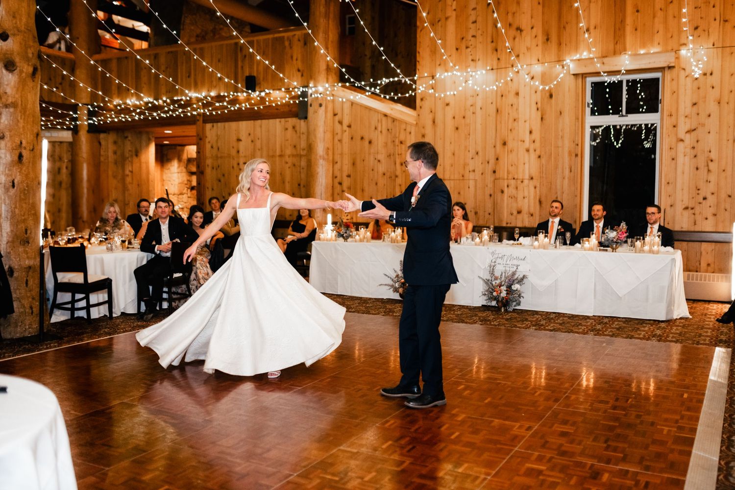 Wedding reception dance in rustic wooden barn decorated with twinkling string lights.