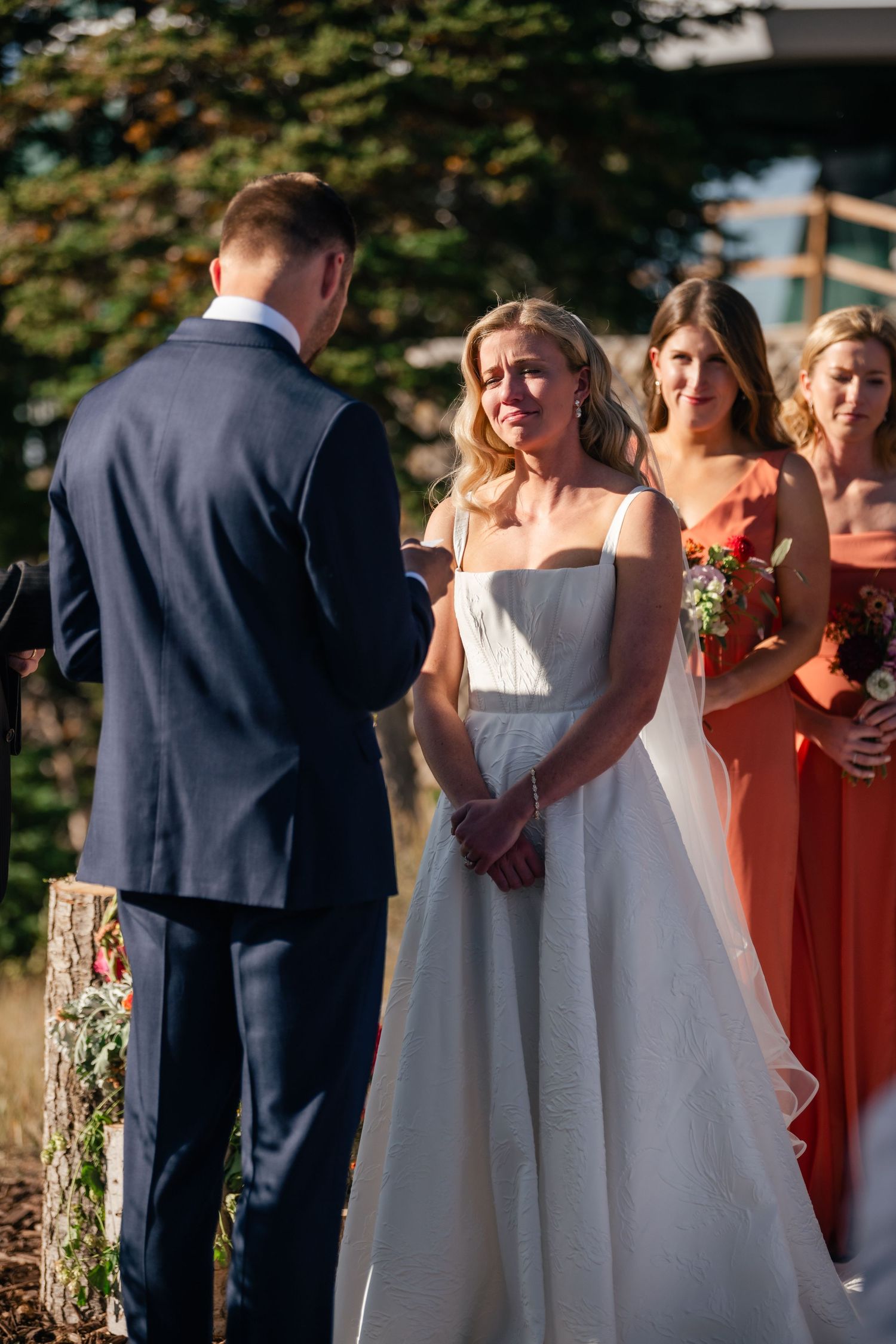 Emotional wedding ceremony moments with bridesmaids in coral dresses and bride in white.