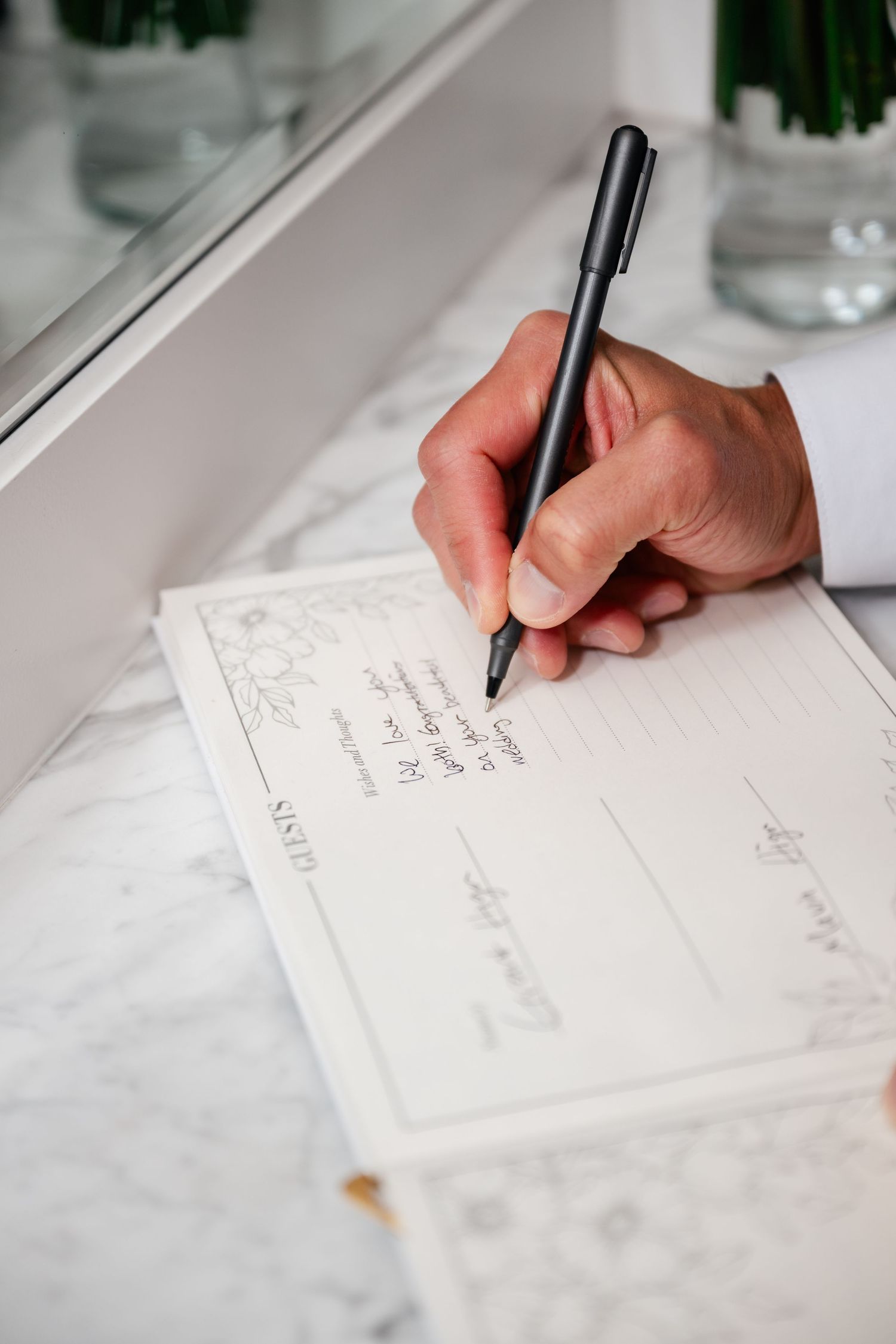 Close-up of hands writing on white paper with elegant black pen.