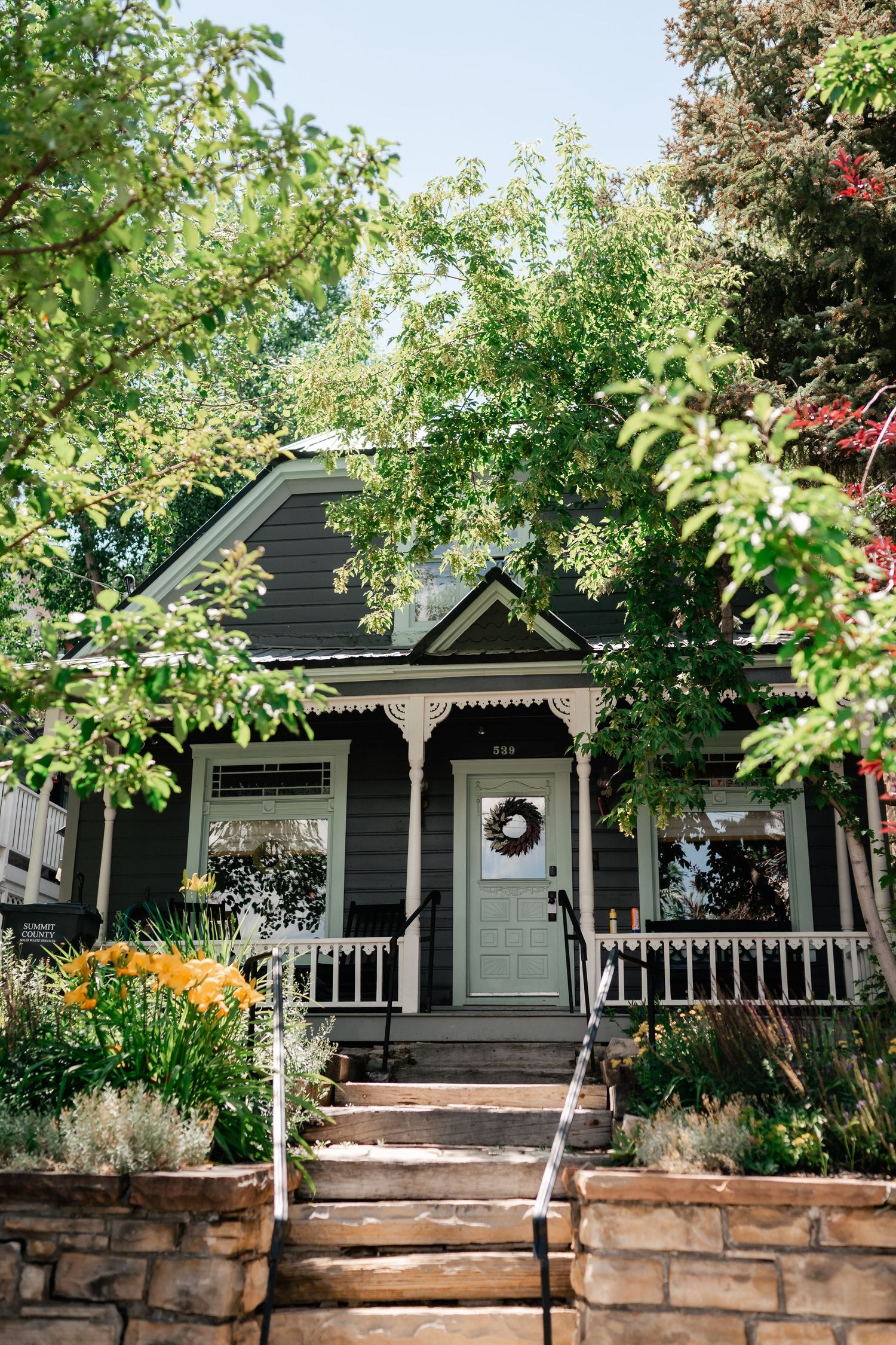Charming cottage-style houses with front porches and stone retaining walls surrounded by lush greenery.