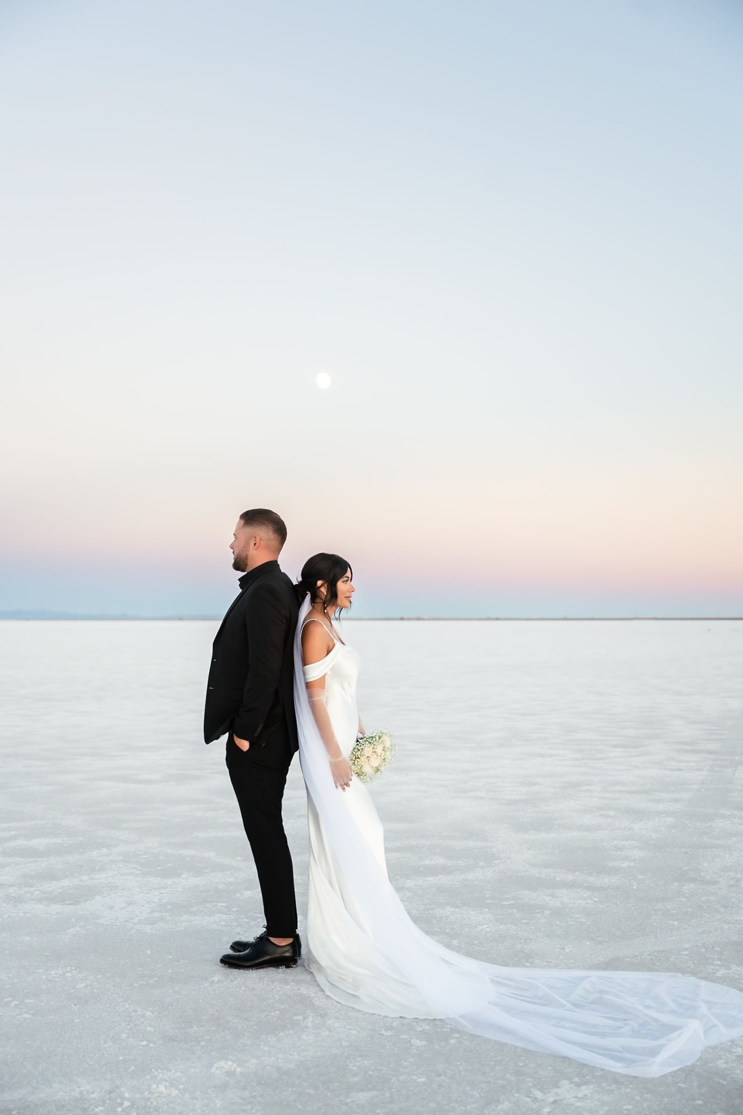 Couple walks together on salt flats during sunset with flowing white wedding dress train.
