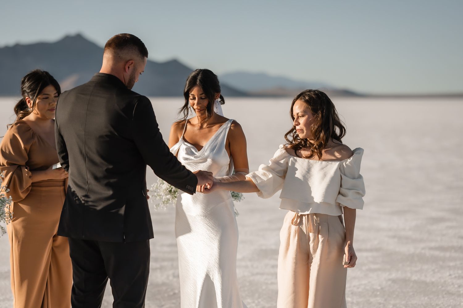A wedding party poses on a scenic salt flat with mountains in the background at sunset.