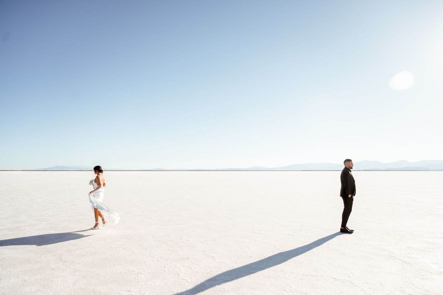 Silhouettes of people standing on a vast white salt flat under blue sky.