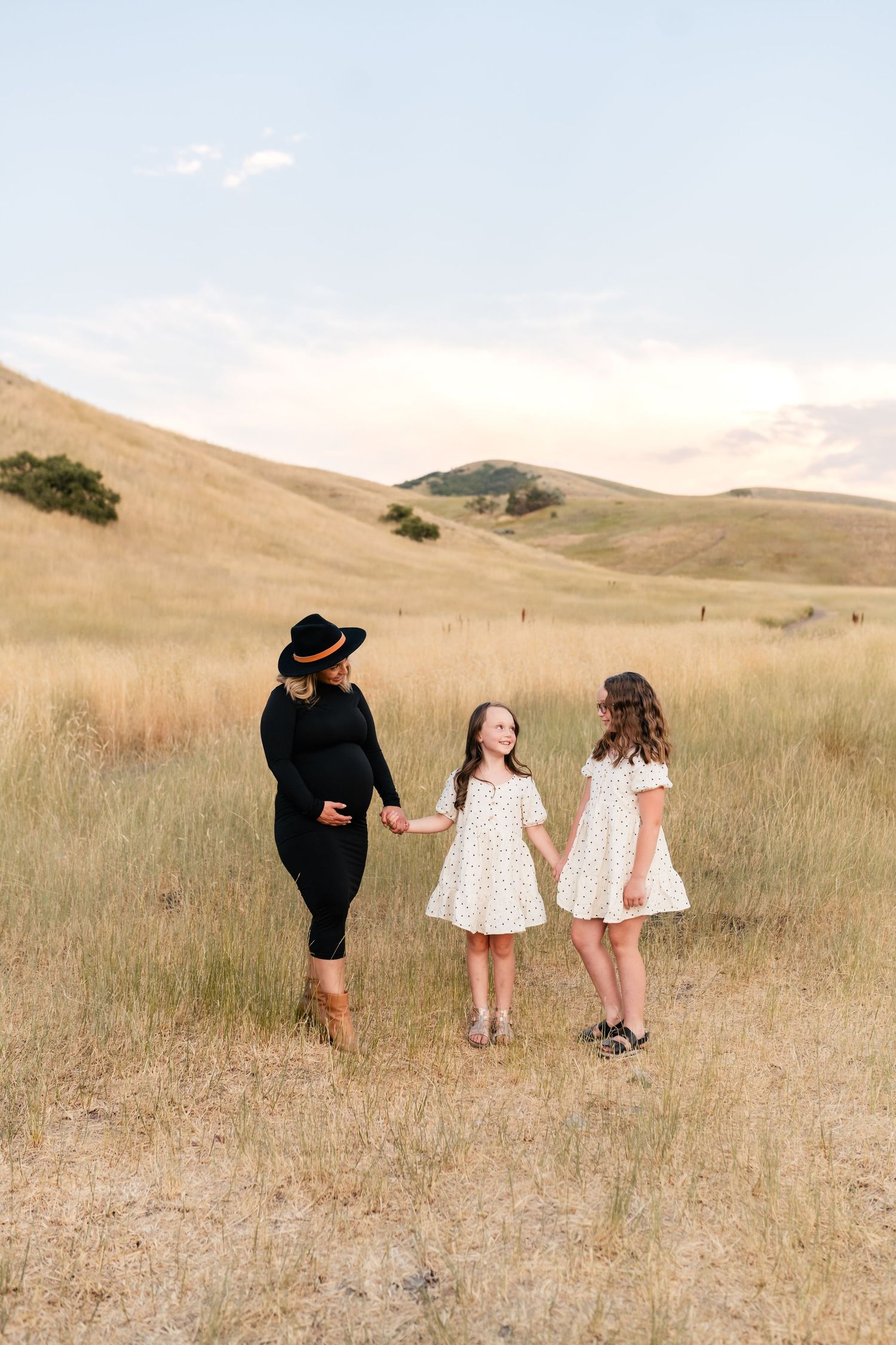 A group stands in a sun-drenched field with rolling hills in the background wearing black and white outfits.