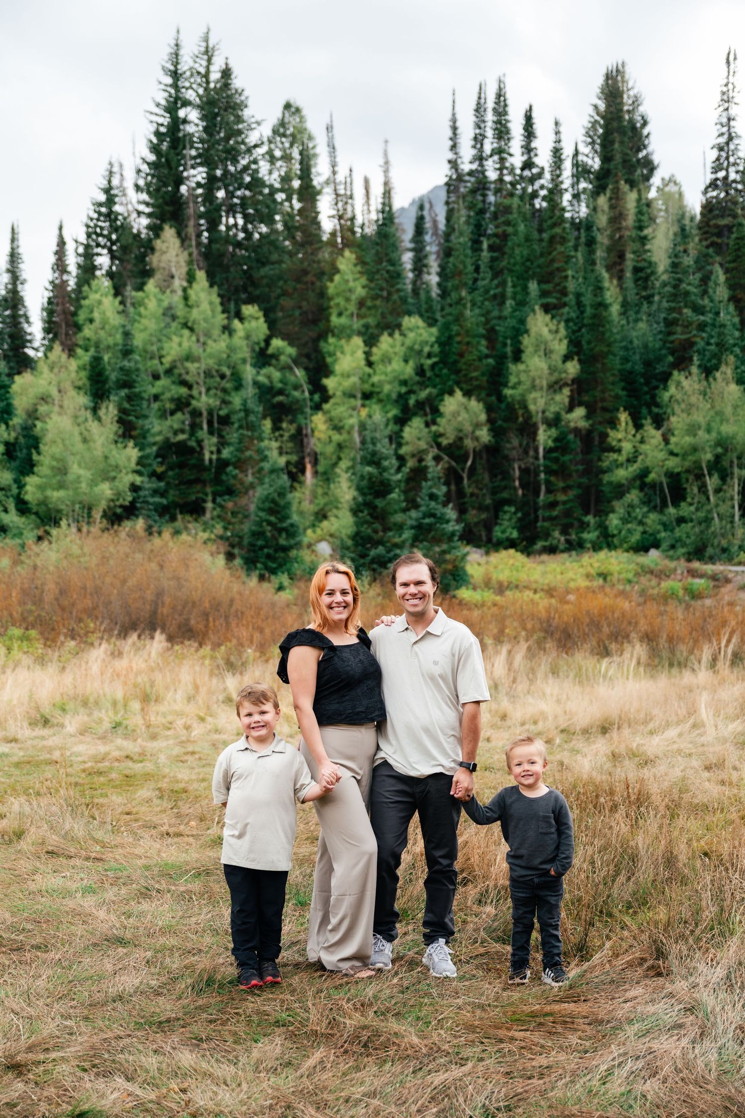 A family group poses together on a hillside with evergreen trees in the background.