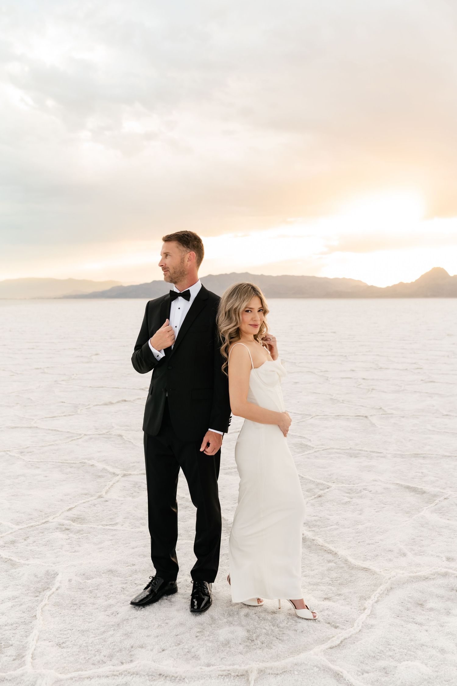 Salt Flats Elopement Photographer. A couple in formal attire poses on the white salt flats at sunset with mountains in the background.