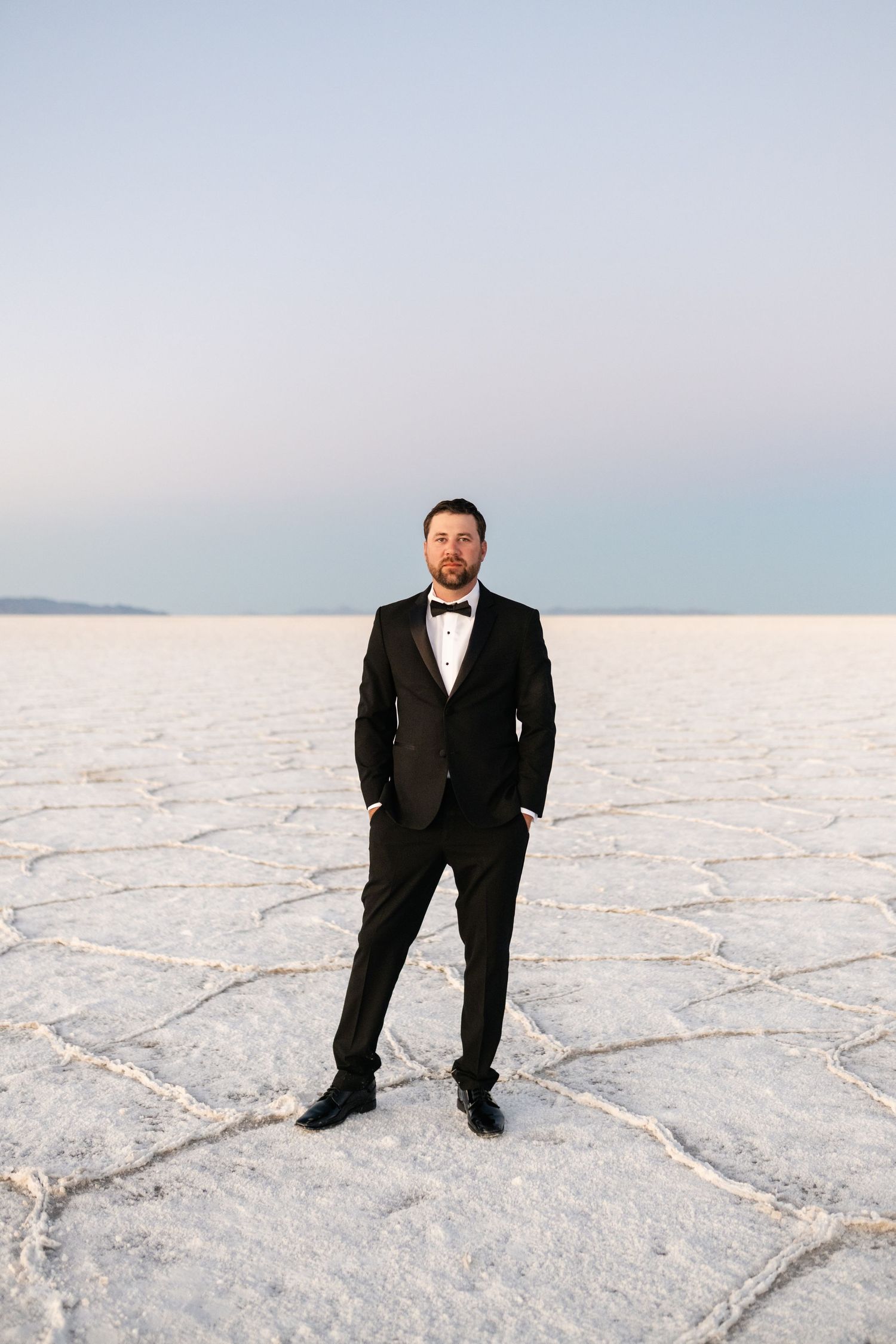 Utah Salt Flats Photographer. Classic tuxedo portrait on the stark white salt flats with mountains in the distance.