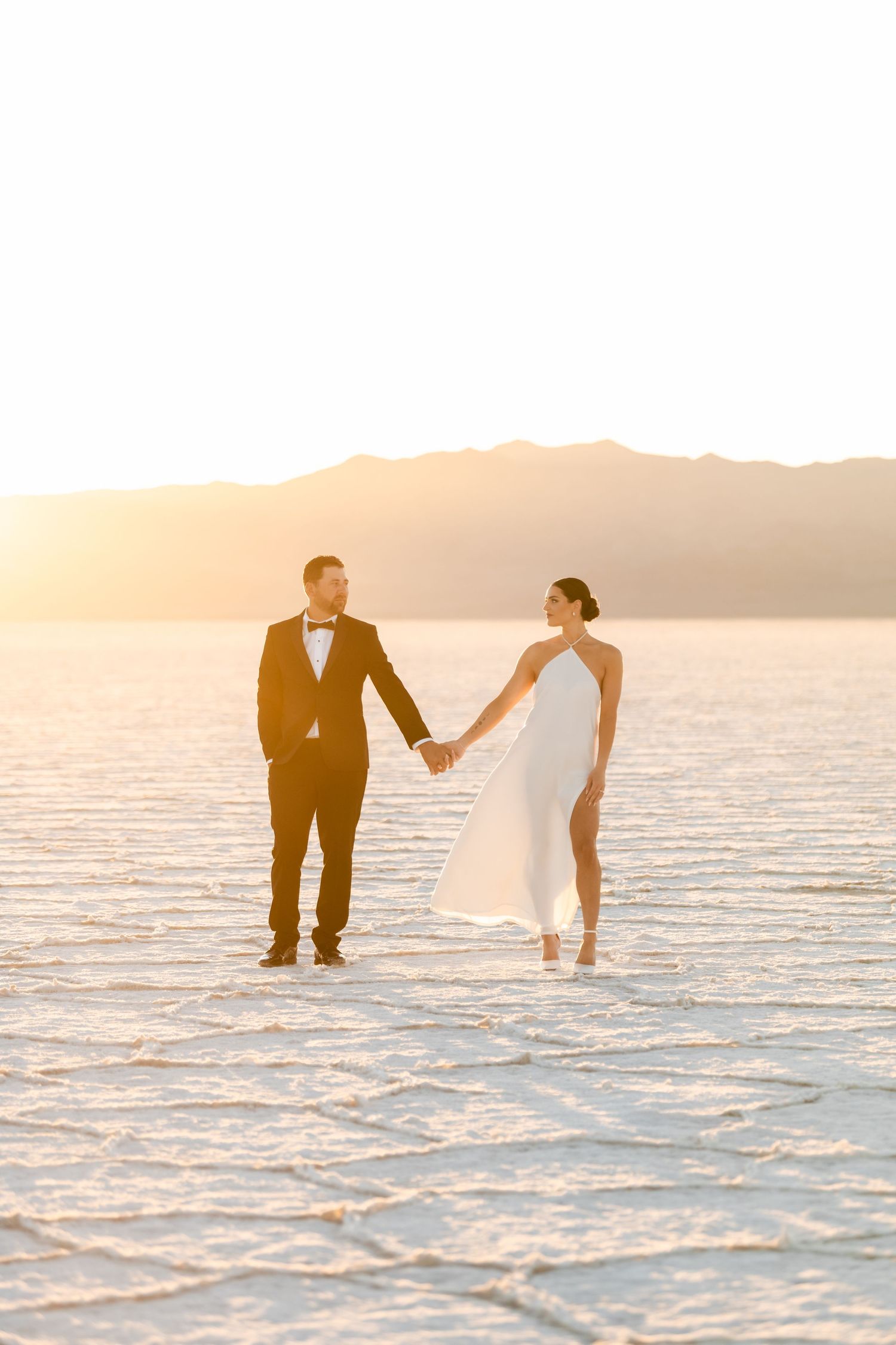 Utah Salt Flats Photographer. A couple in wedding attire holds hands while standing on salt flats during golden hour sunset.