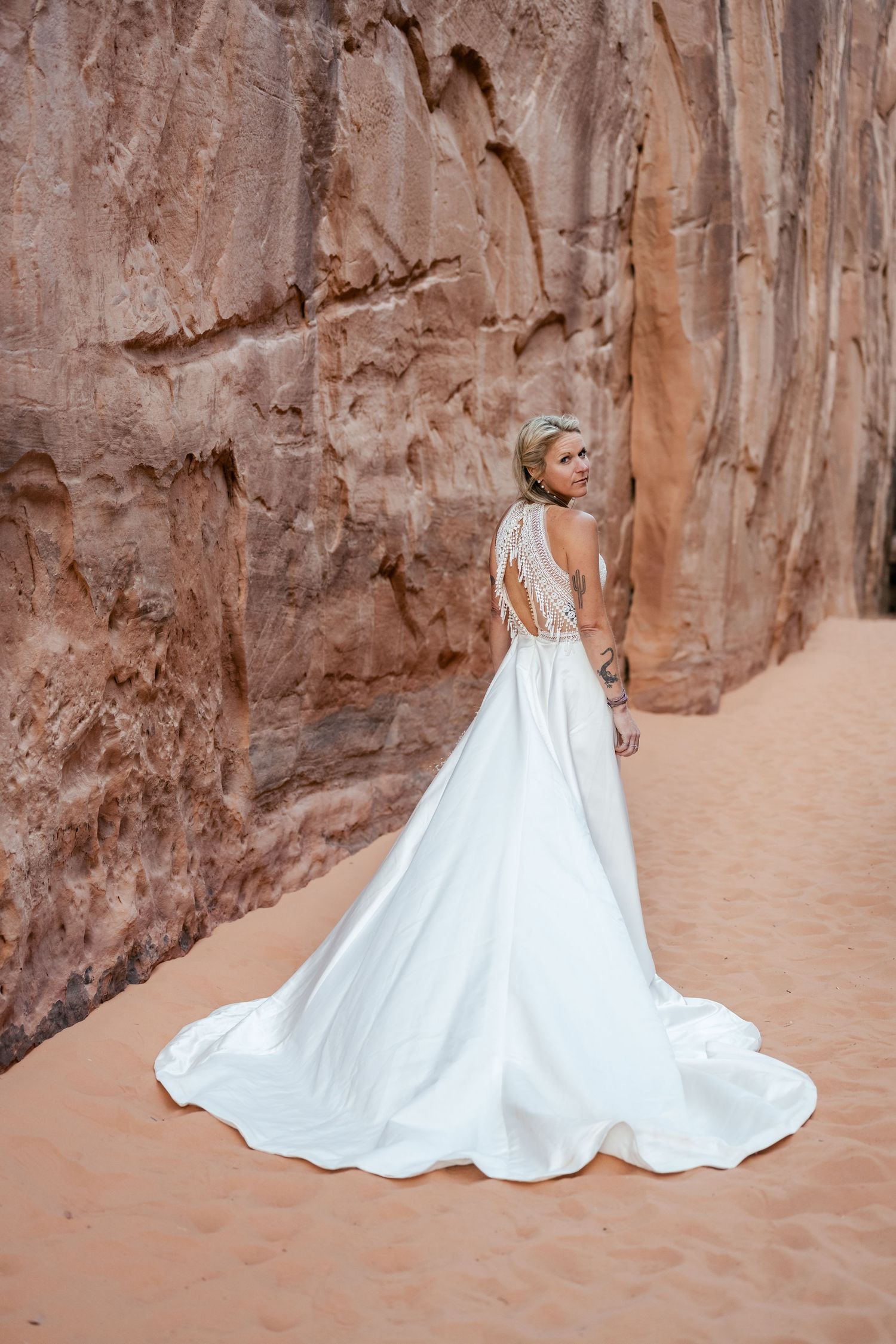 A flowing white wedding dress train trails elegantly against red desert canyon walls.