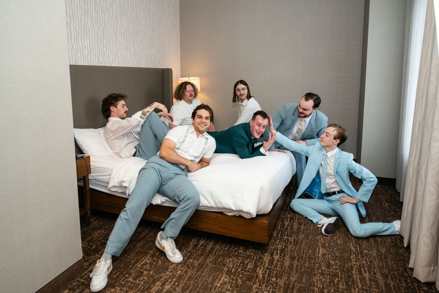 A group wearing matching blue attire lounges casually on a hotel room bed in a playful pose.