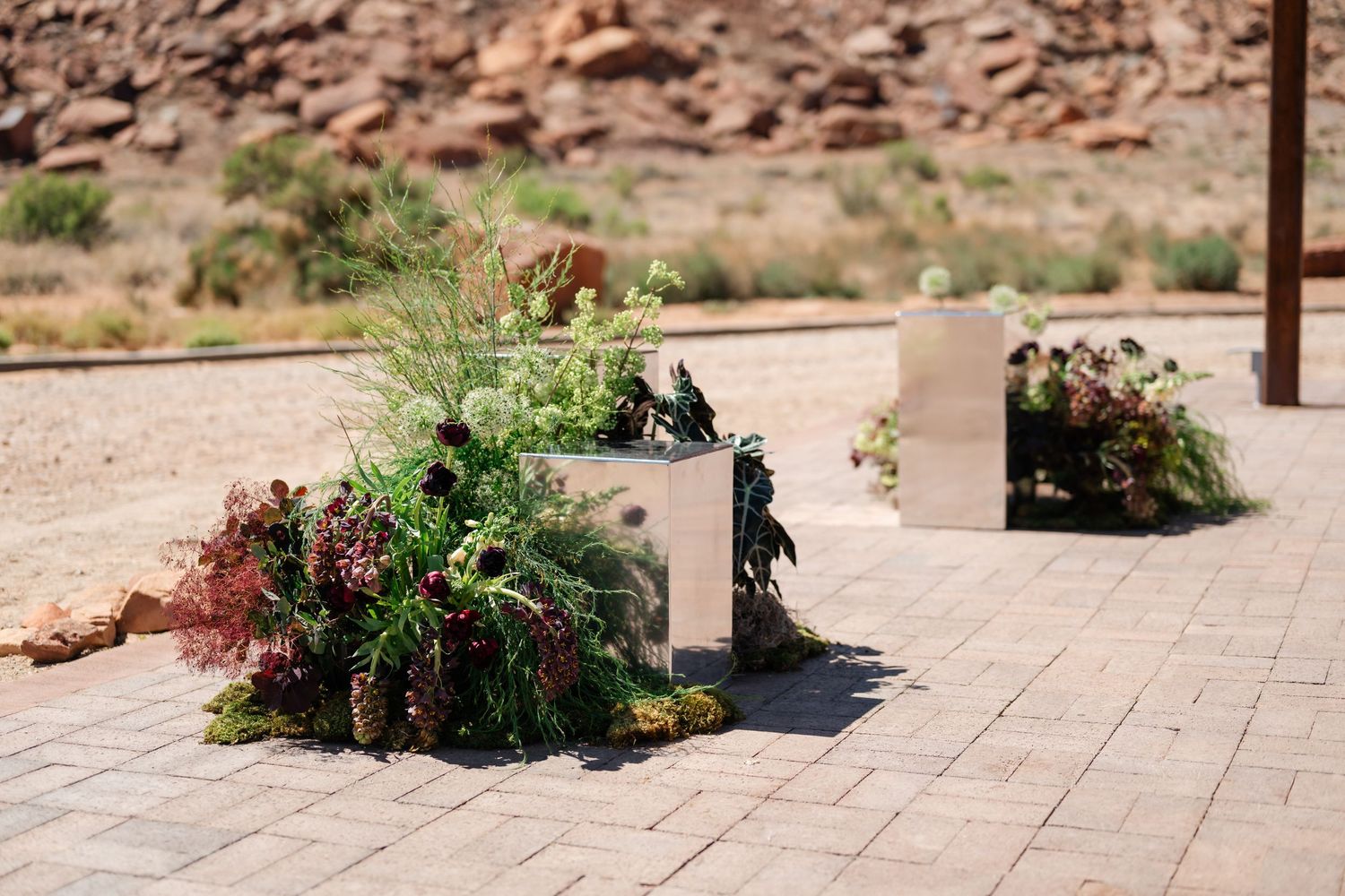 Desert patio with lush green and red succulent arrangements in metallic planters against rocky landscape.