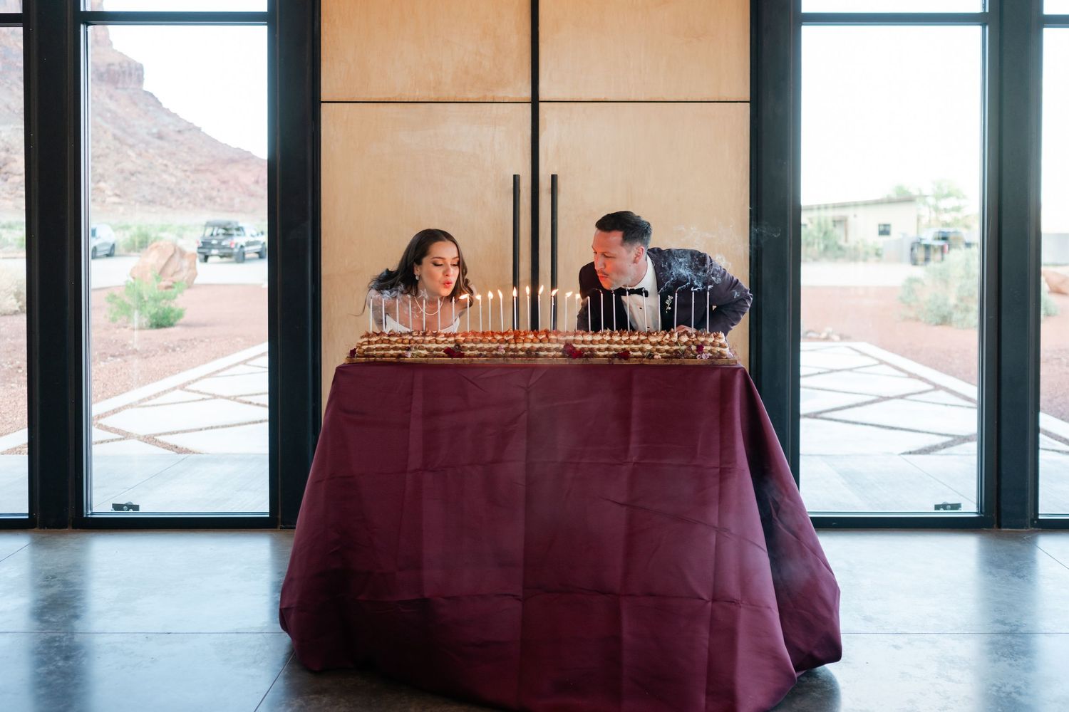 Couple leaning over a burgundy-draped table with candles and appetizers in a modern venue with desert views.
