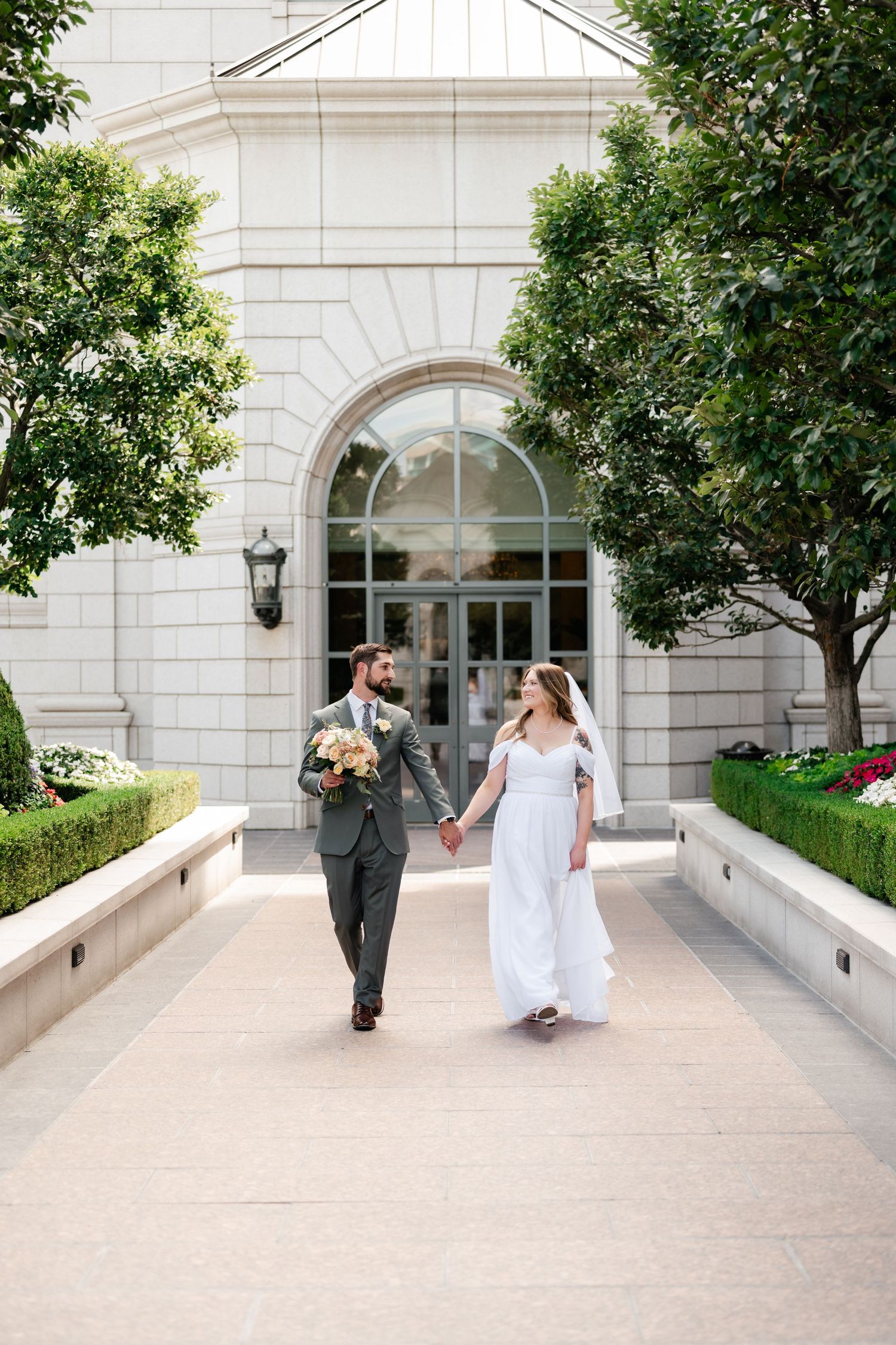 A sequence of wedding photos capturing a couple walking along a white stone pathway with trees and landscaping.