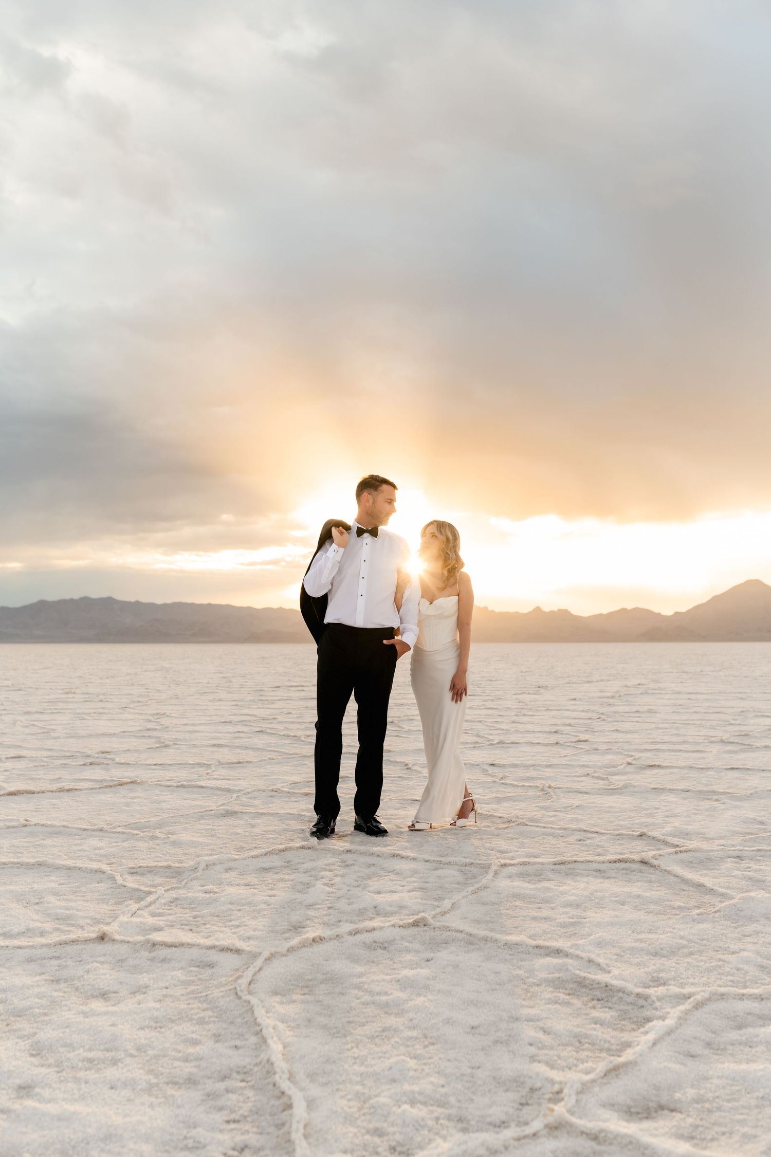 A couple walks together across the white salt flats at sunset with mountains in the distance. Salt Flats Photographer.