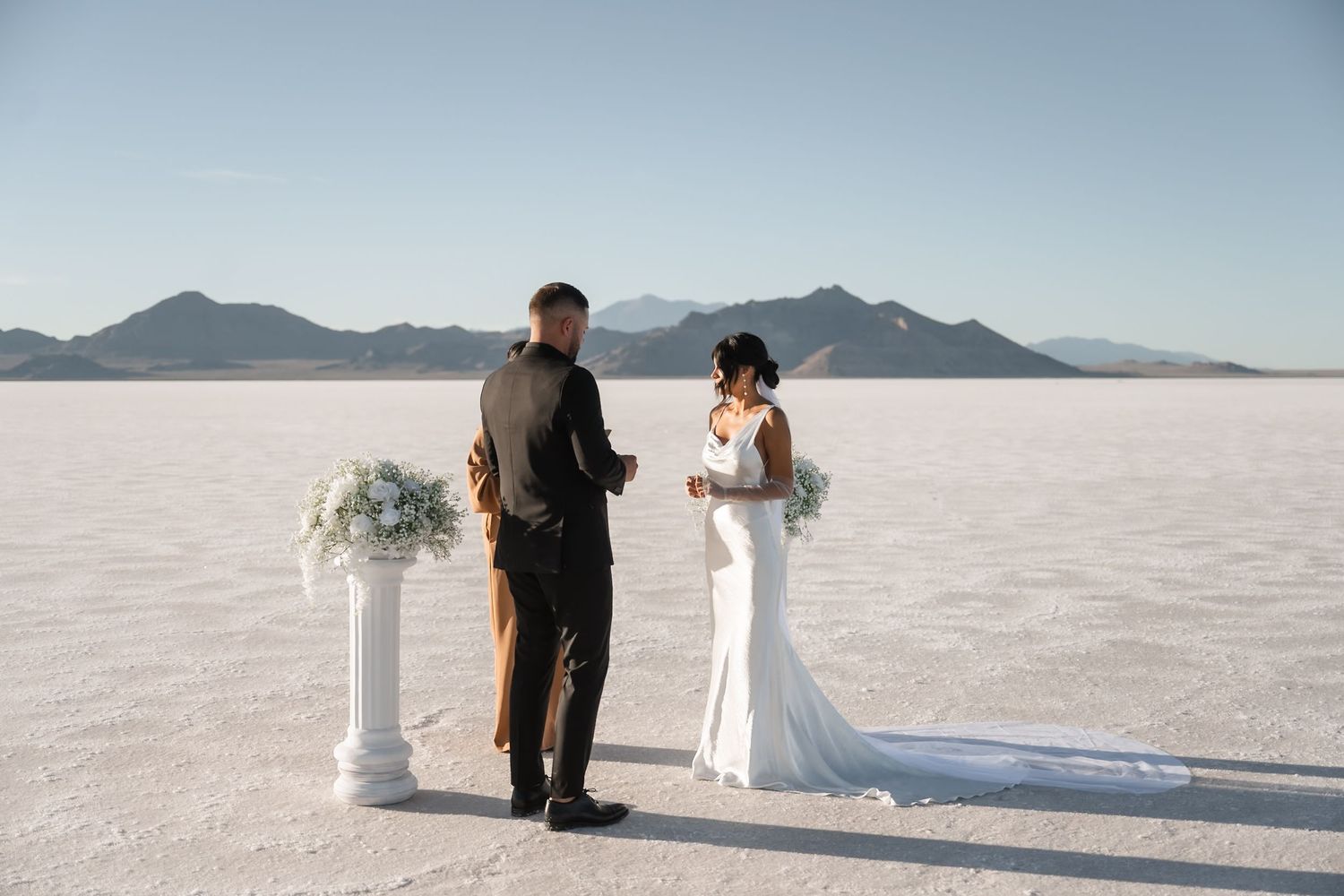 Wedding ceremony setup with white columns and flowers against vast salt flats landscape.