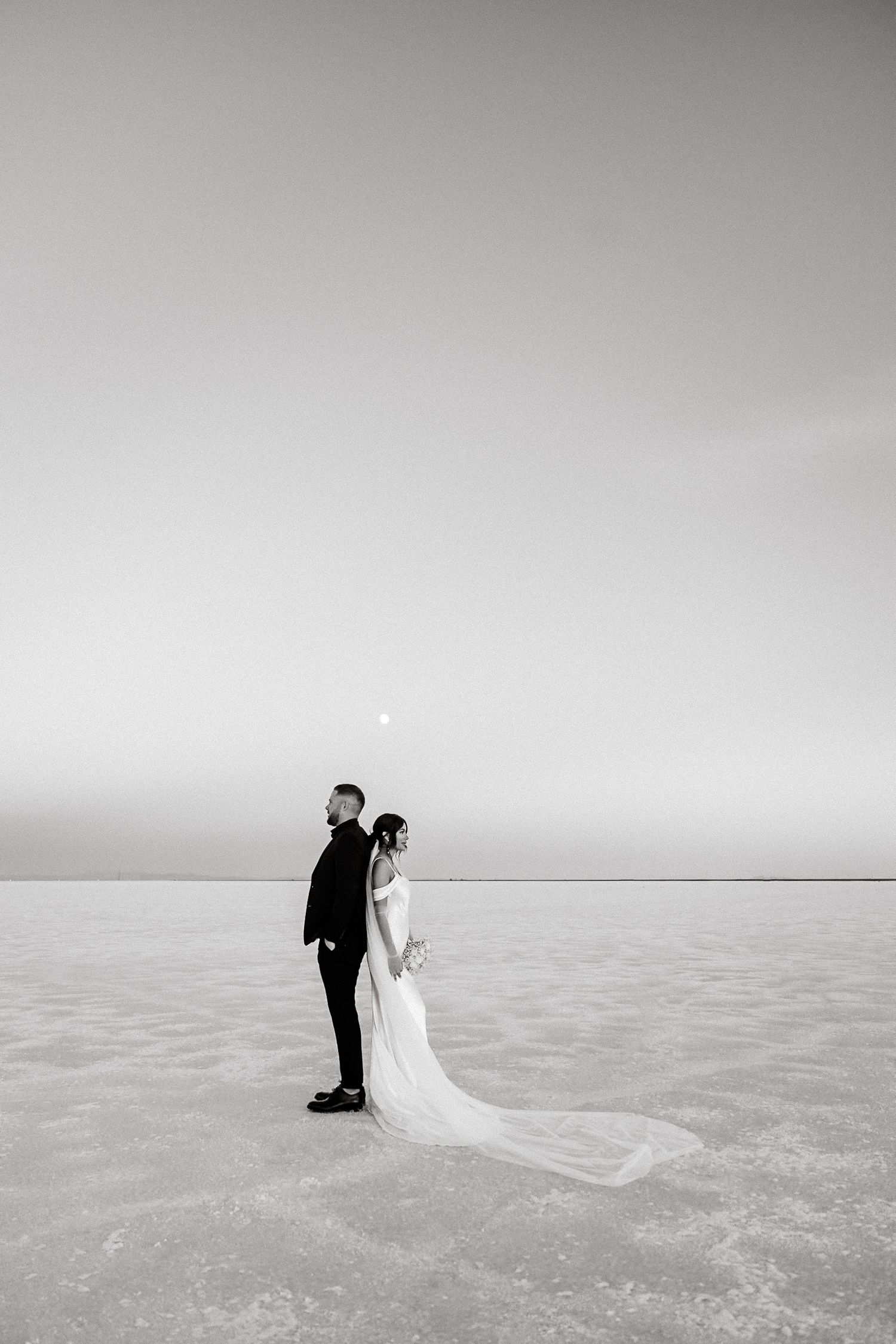 A dramatic black and white photo of a couple on an expansive salt flat.