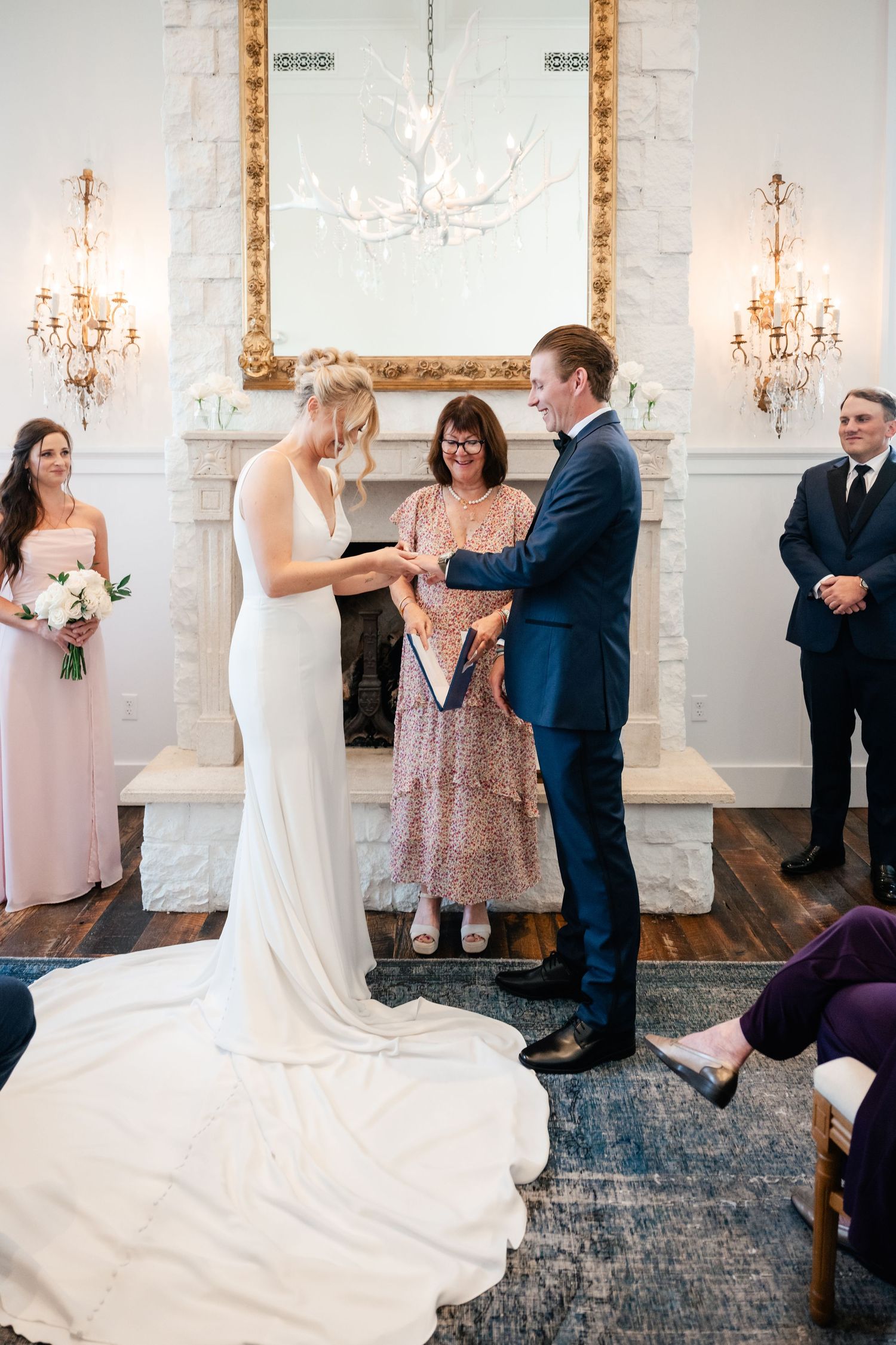 Wedding party dancing and celebrating in an elegant reception room with white walls and crystal chandeliers.