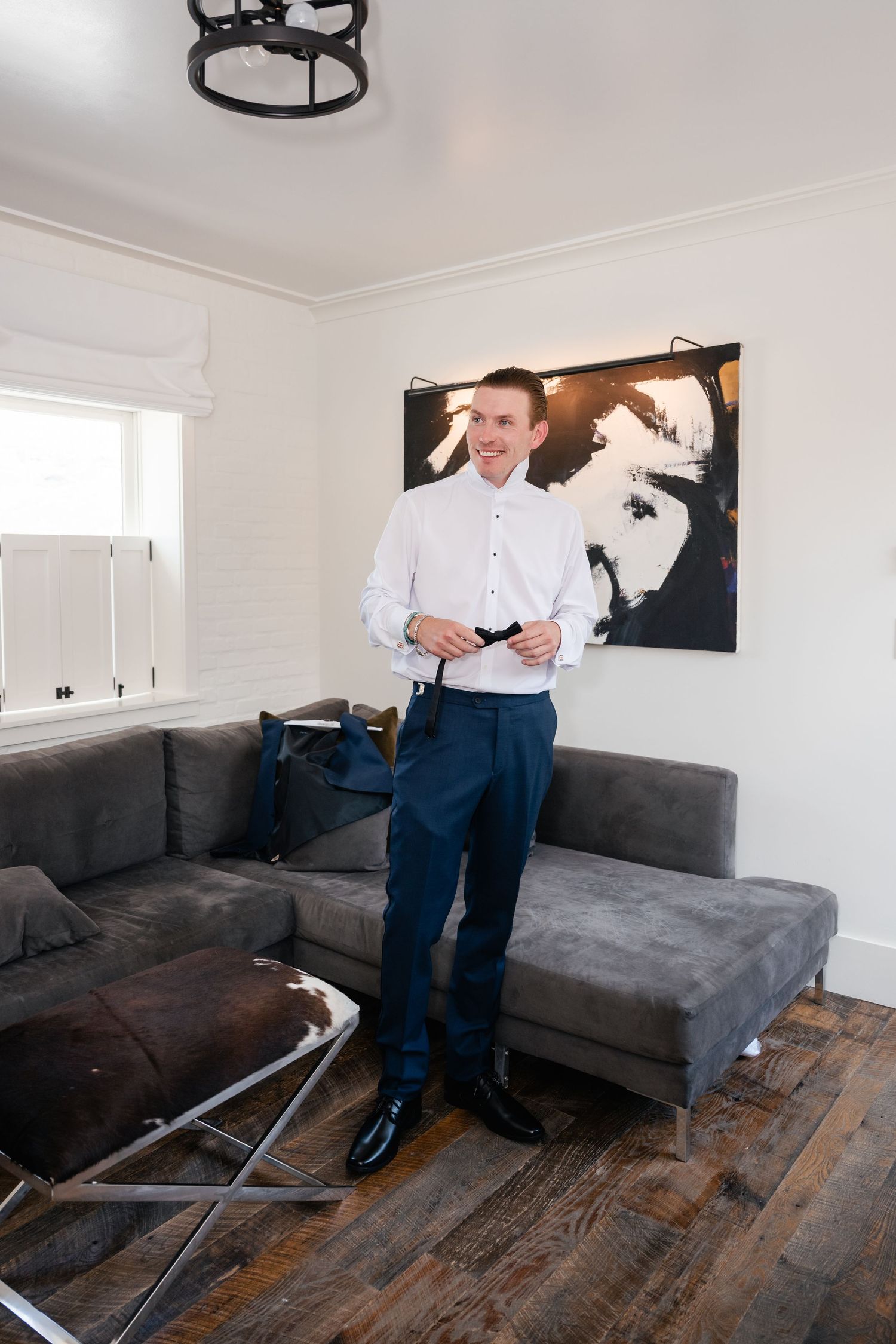 Person in formal navy suit and bow tie adjusting outfit in living room.