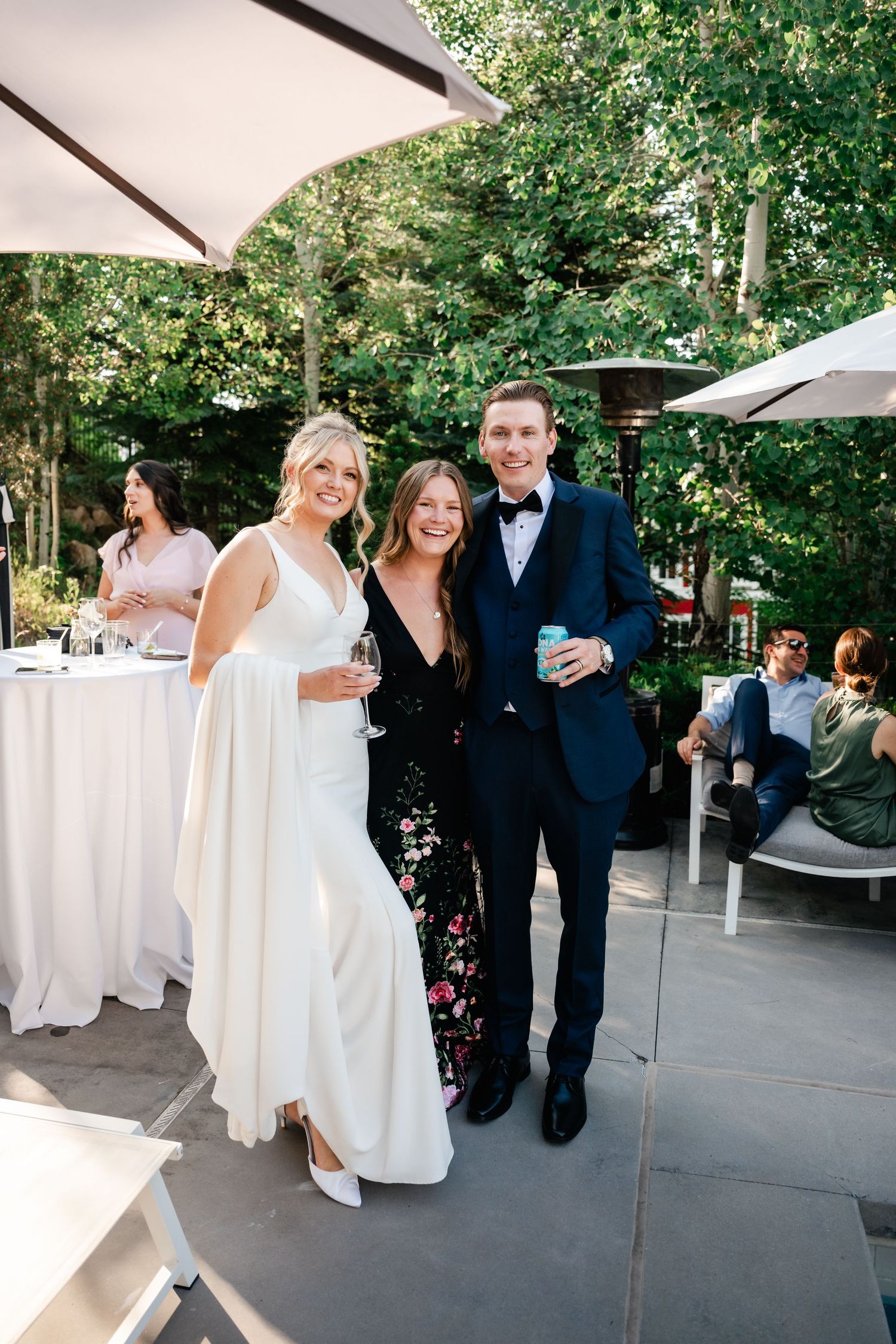 Wedding guests mingle on an outdoor patio with white decor and natural greenery.