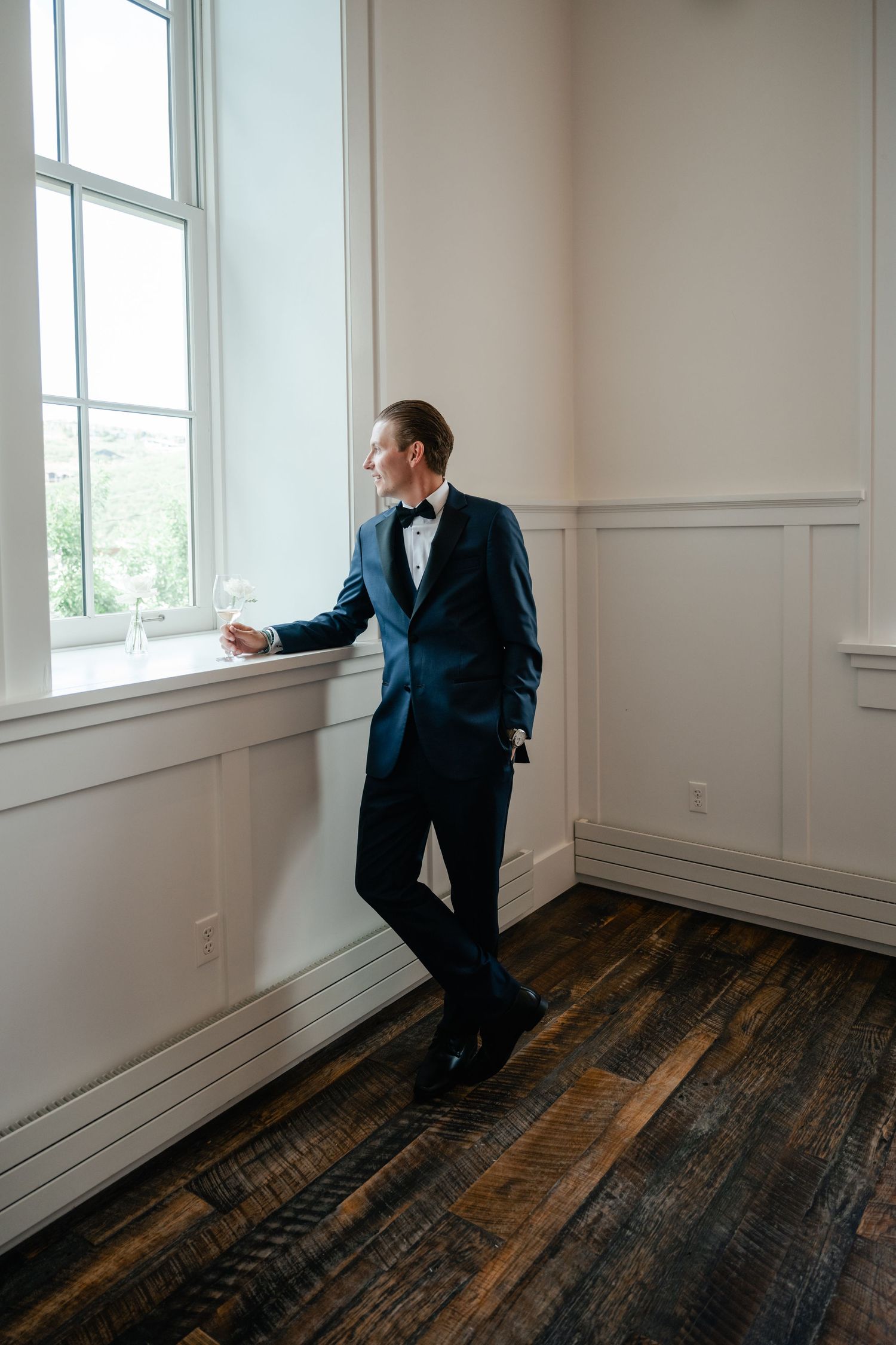 Empty room interior with white walls, baseboards and dark hardwood flooring near bright windows.