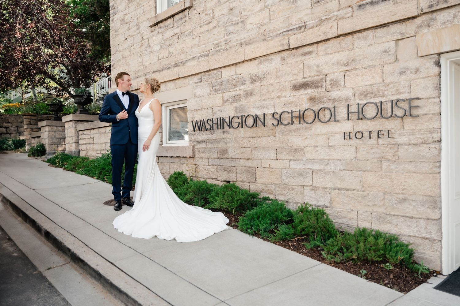 A couple poses outside a historic stone building with Washington School House Hotel signage.