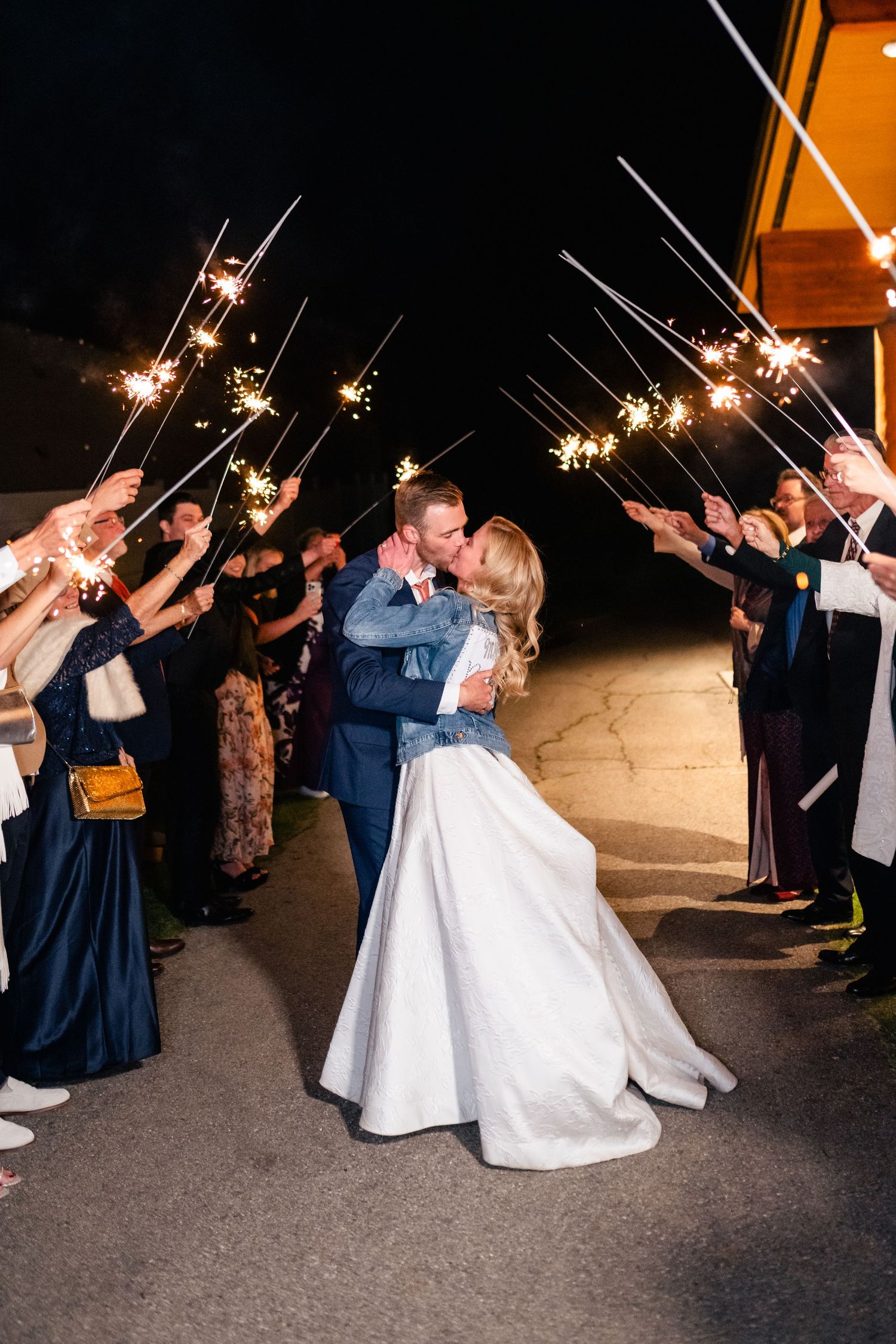 Wedding party celebrates with sparklers creating a magical nighttime send-off outside the venue.