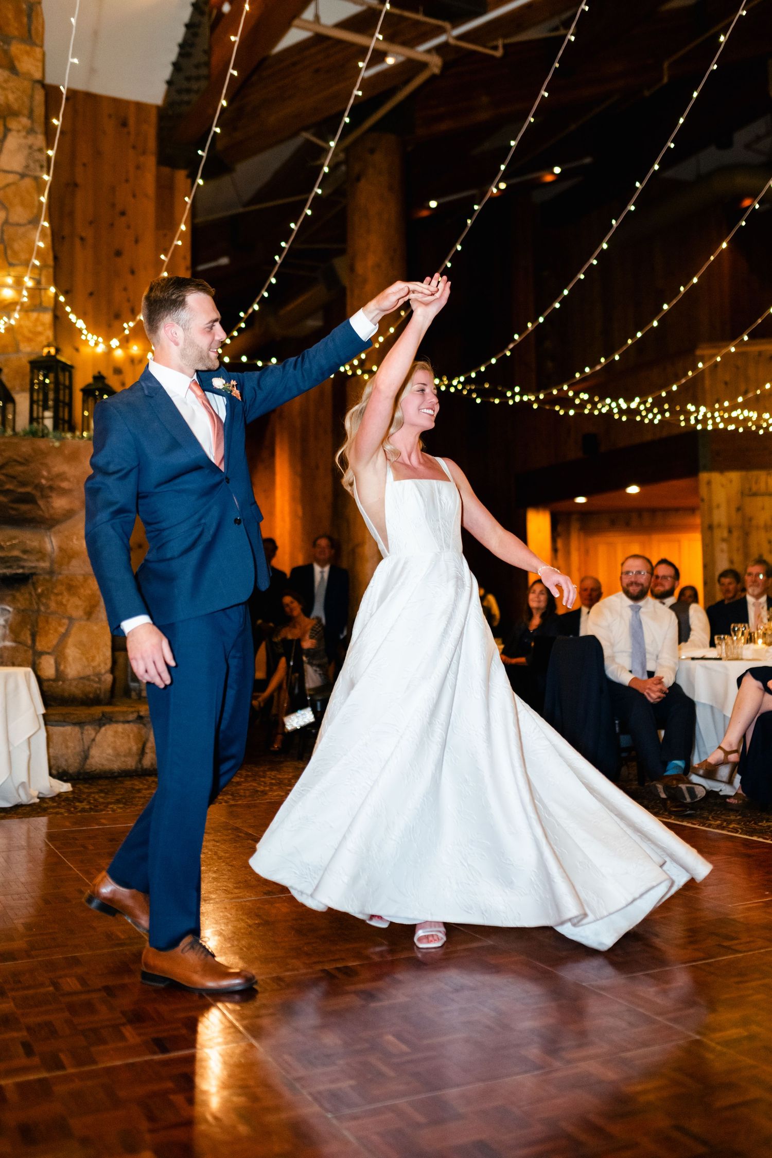 Dancing couple twirling on a rustic wooden dance floor under string lights at a wedding reception.