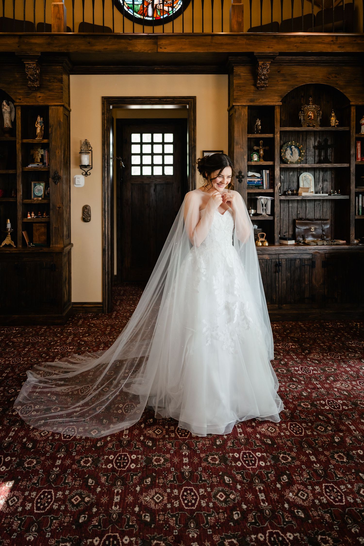 Wedding dress with long train displayed in ornate room with stained glass and dark wood details.