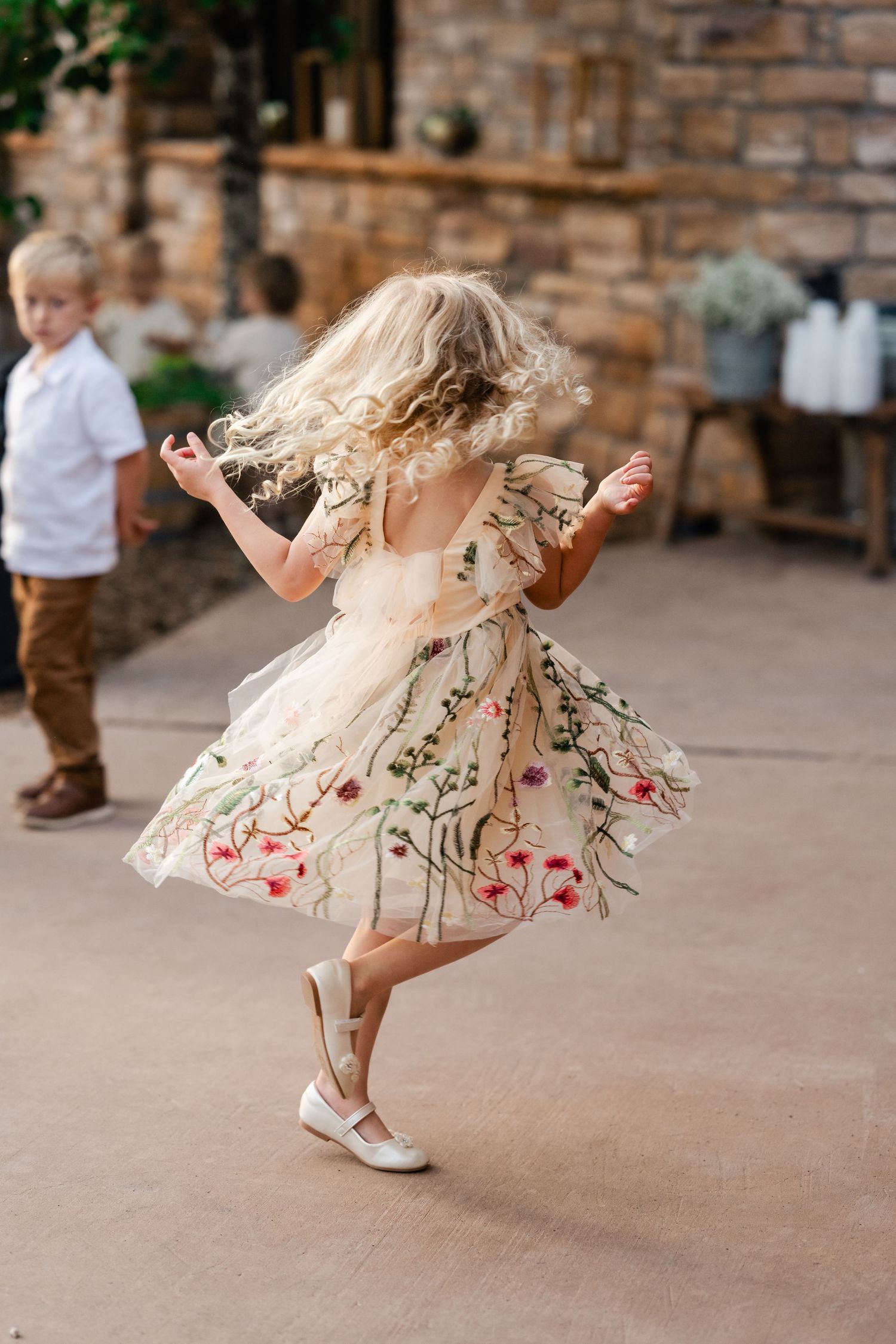 A young child twirls in a floral dress on a concrete patio during a celebration.