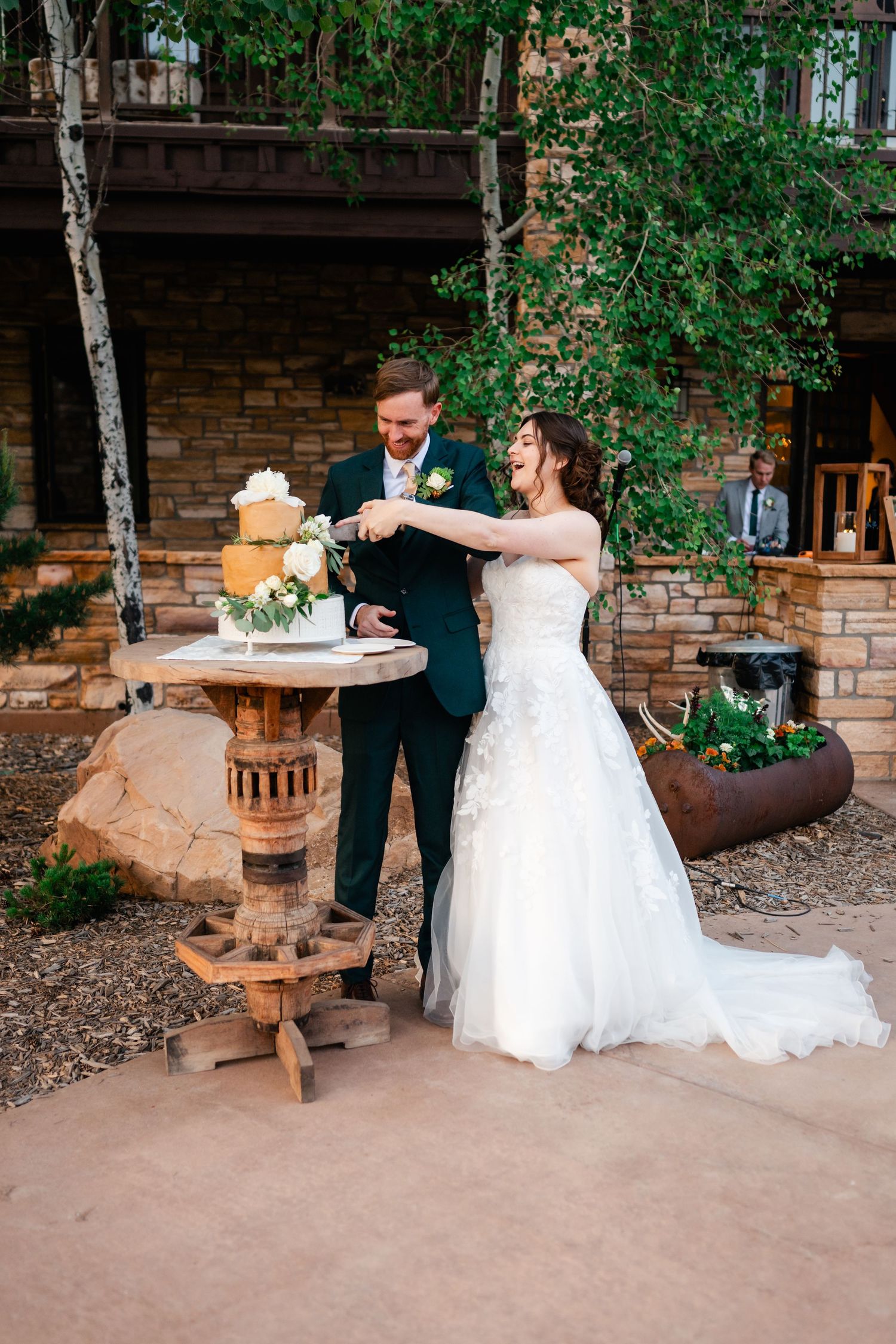 A couple performs their first dance outdoors with brick walls and trees in the background.