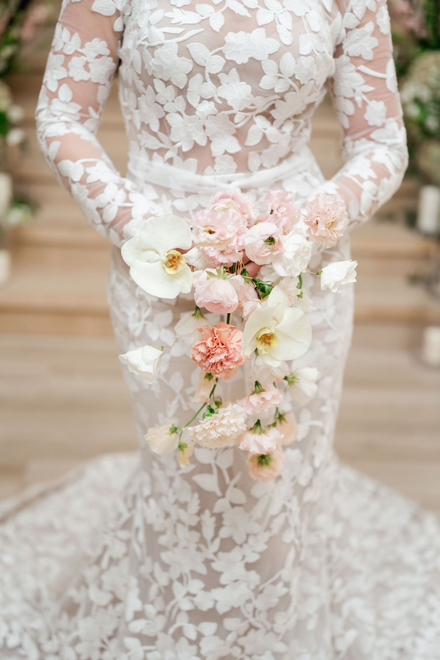 Close-up details of a white lace wedding dress with delicate floral appliques and soft pink flower bouquet accents. Wedding details.