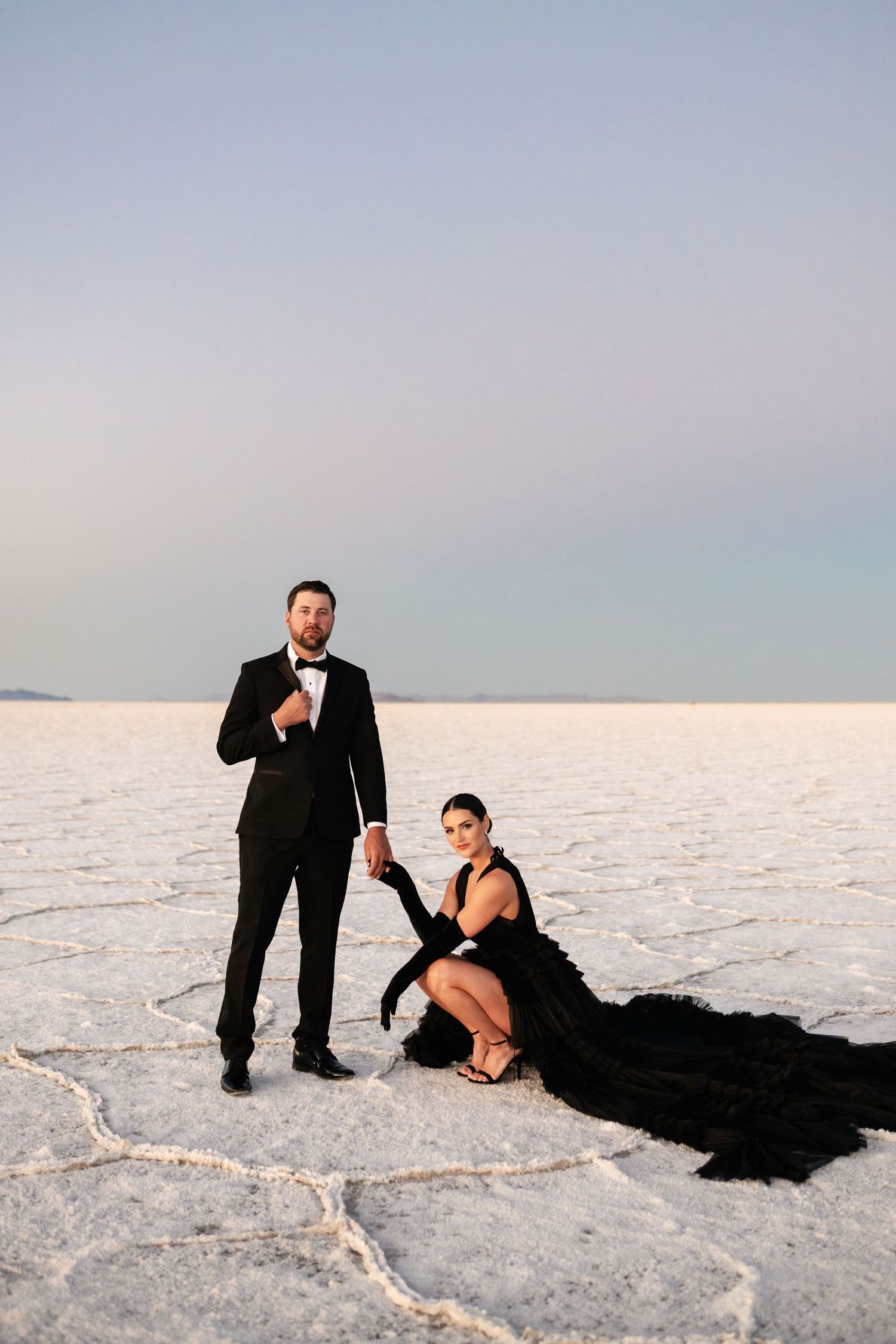 Utah Salt Flats Photographer. Stylish couple in formal attire poses on salt flats with dramatic black dress train.