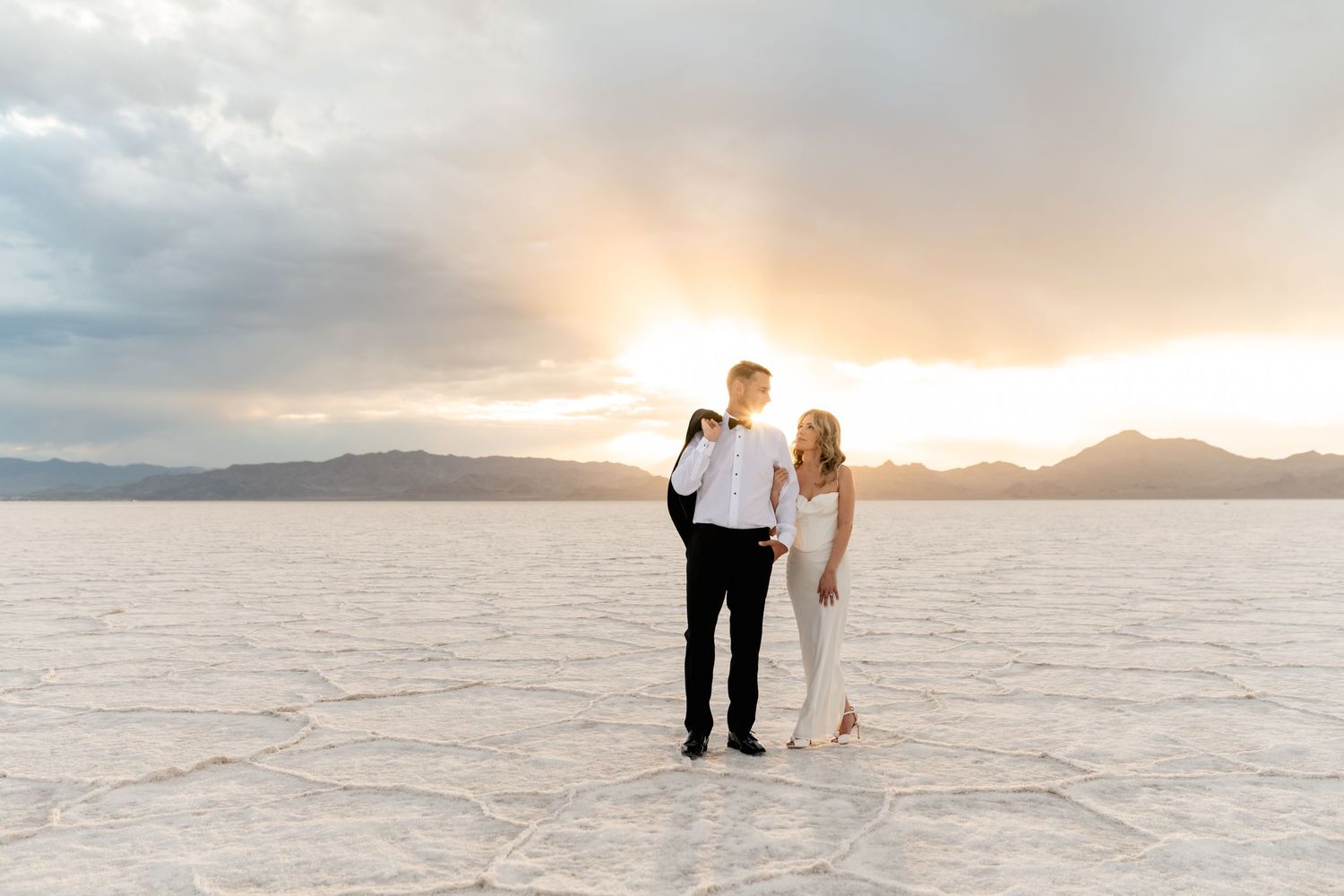 A couple walks hand in hand across the salt flats at sunset creating a dreamy silhouette against the pink sky. Salt Flats Elopement Photos.