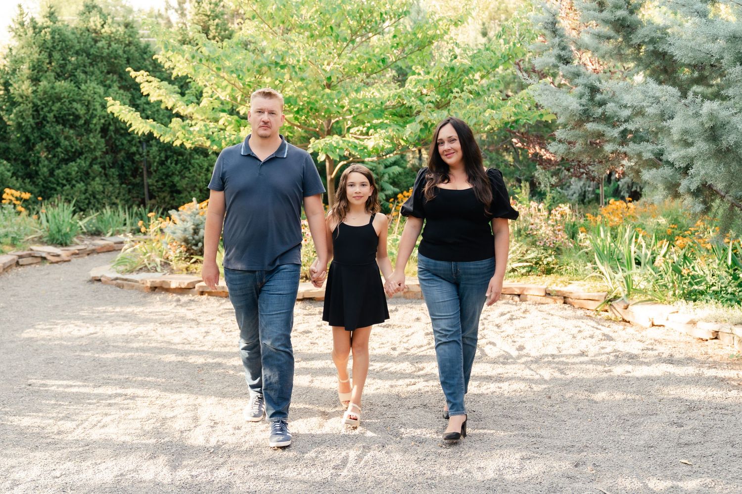 Three people walk together on a sandy path through a garden setting in casual attire.