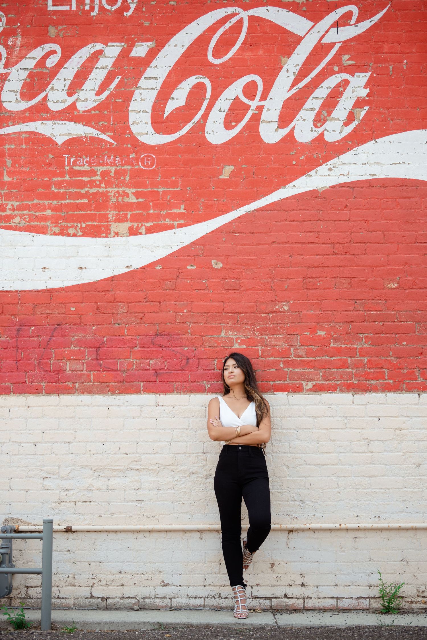 A series of artistic poses photographed against a vintage Coca-Cola mural painted on a brick wall.