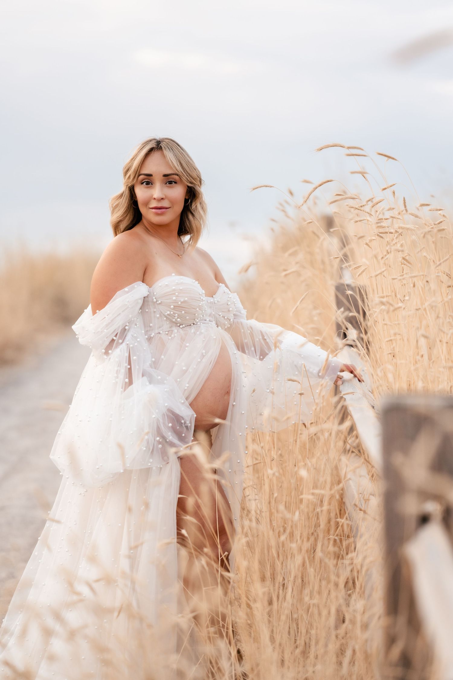 Ethereal portrait in a golden wheat field featuring a flowing white off-shoulder dress and soft natural lighting.