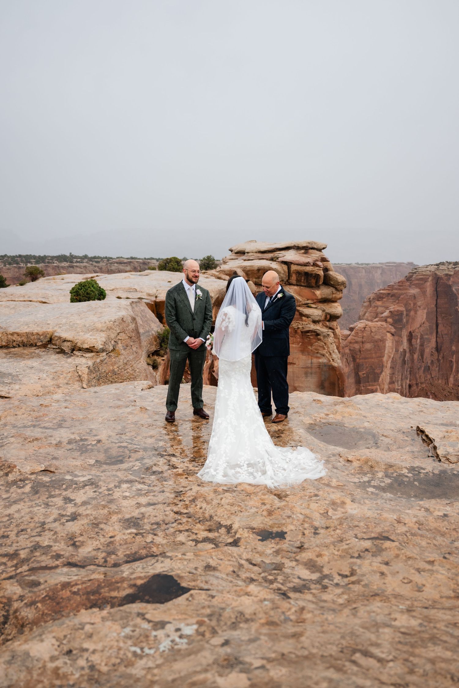 Wedding party gathered on rocky desert overlook with dramatic canyon views in background.