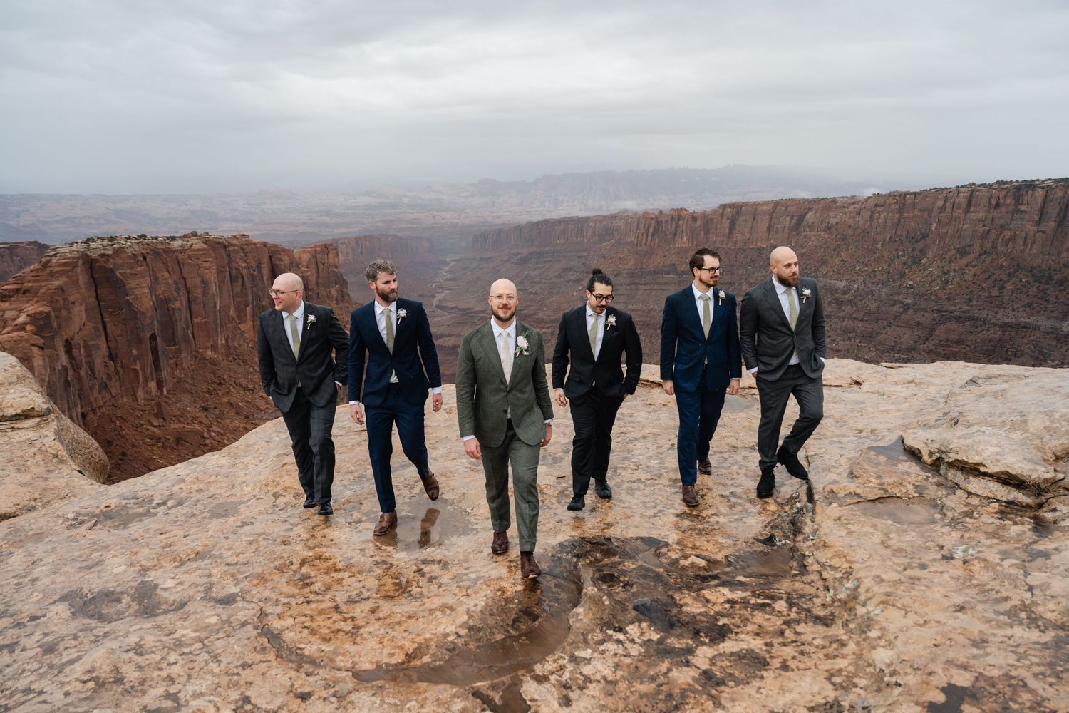 Wedding party members in formal attire pose along dramatic canyon rim.
