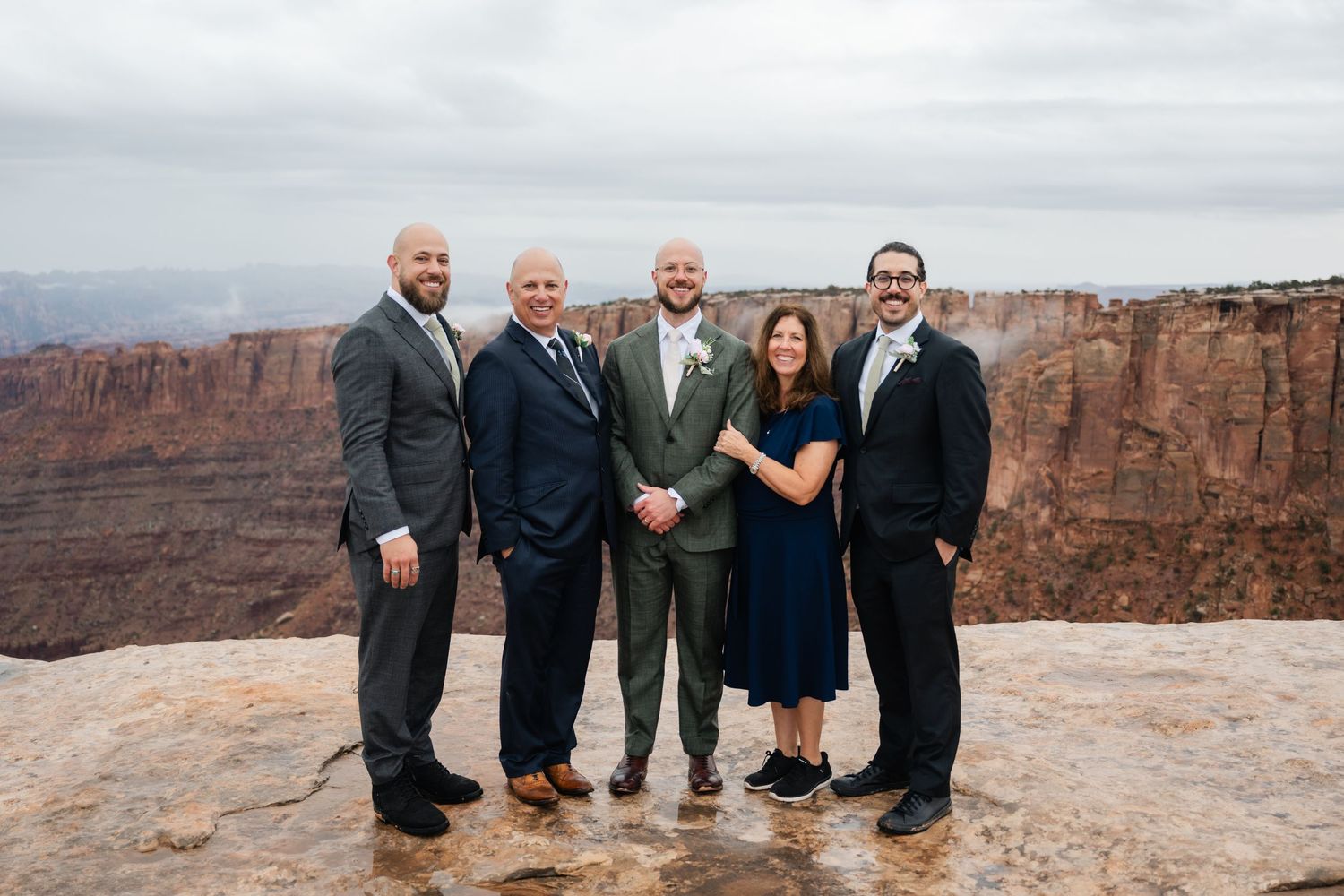 A small group poses together at the edge of a scenic desert canyon overlook under overcast skies.