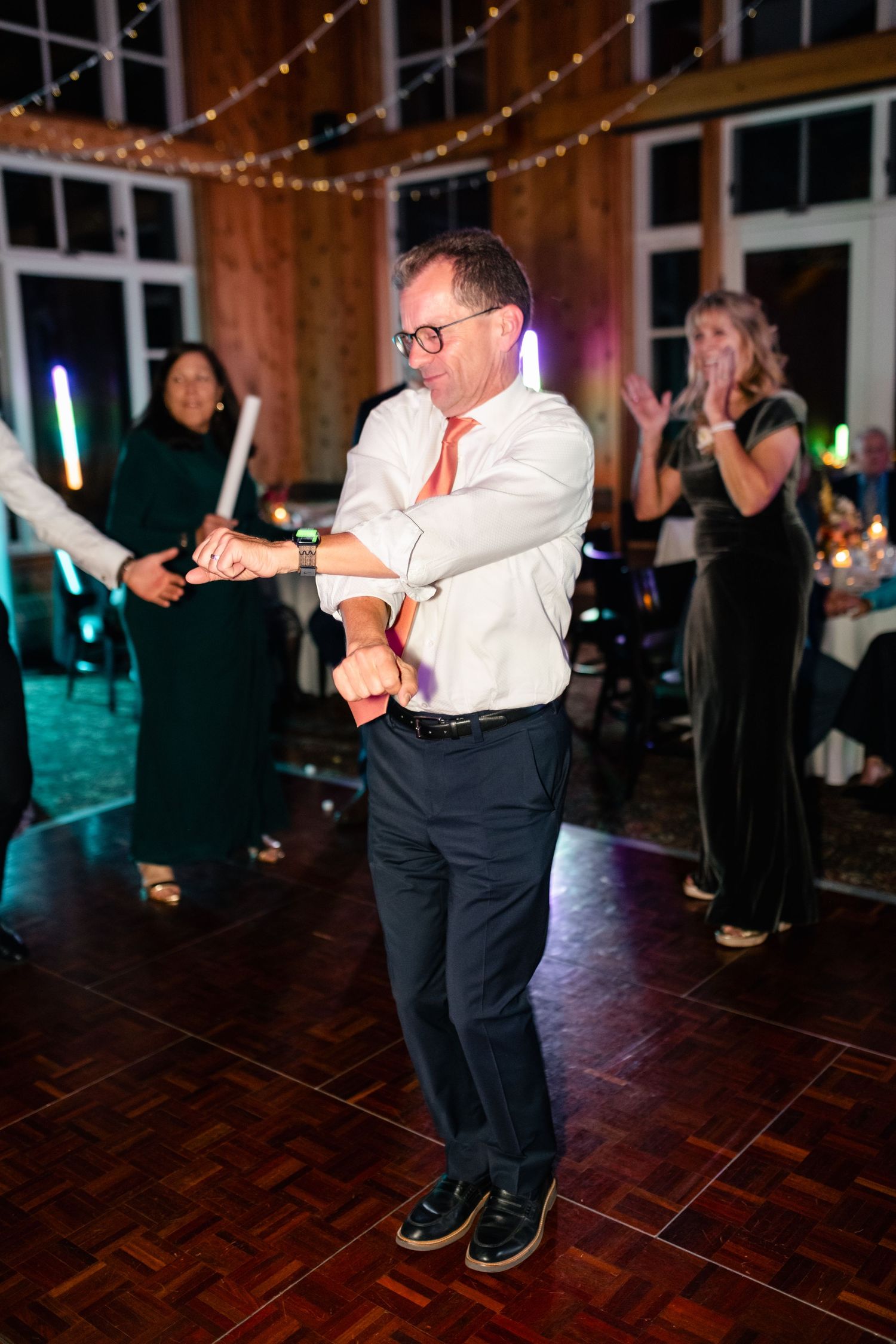 Wedding guest dancing solo on wooden dance floor under string lights at reception.