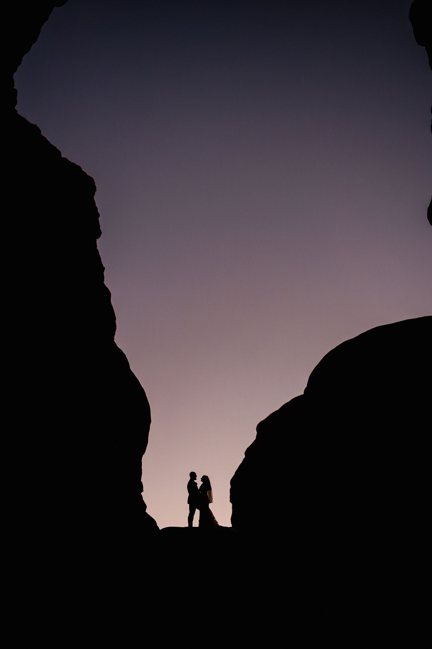 Silhouette of couple between rock formations at twilight.