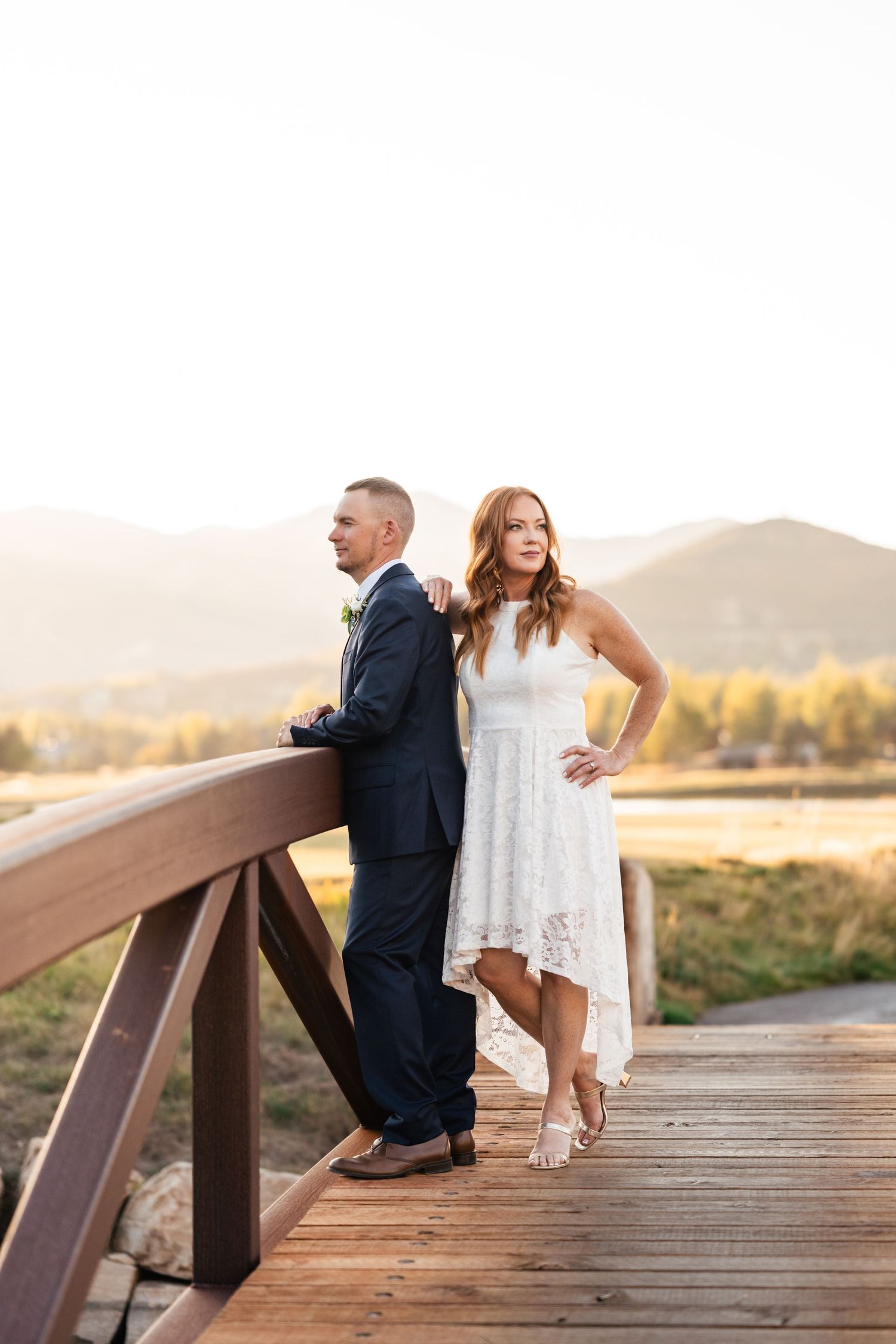 A couple sits together on a wooden deck overlooking mountains at sunset.