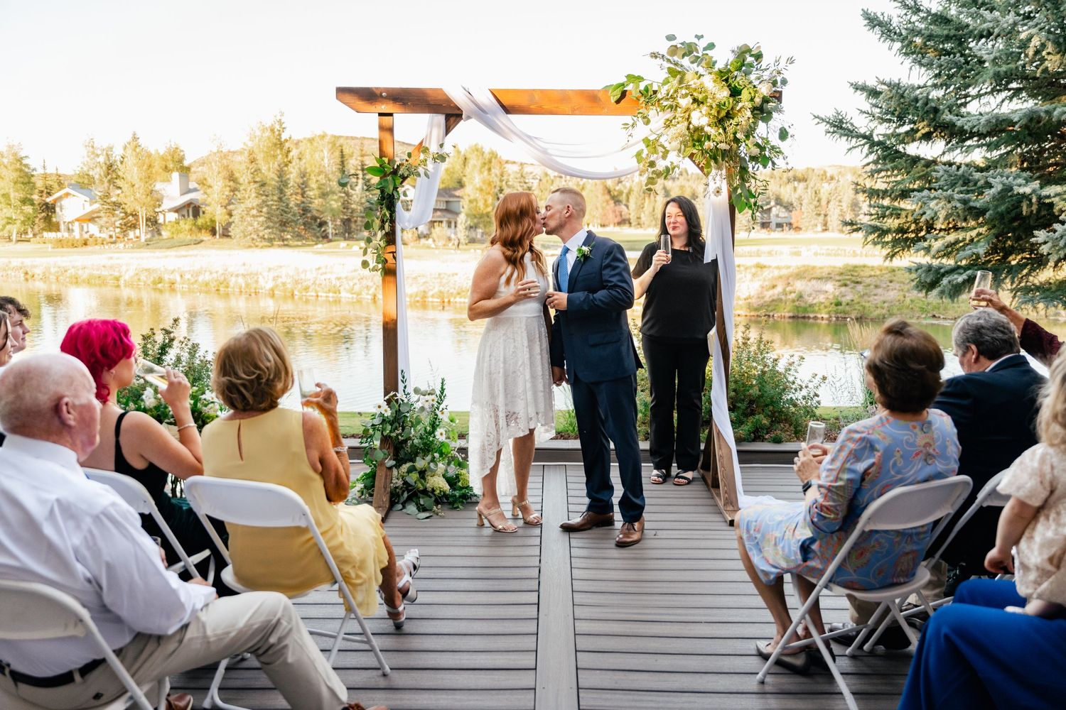 Guests enjoy outdoor wedding celebration on spacious deck surrounded by natural scenery and pine trees.