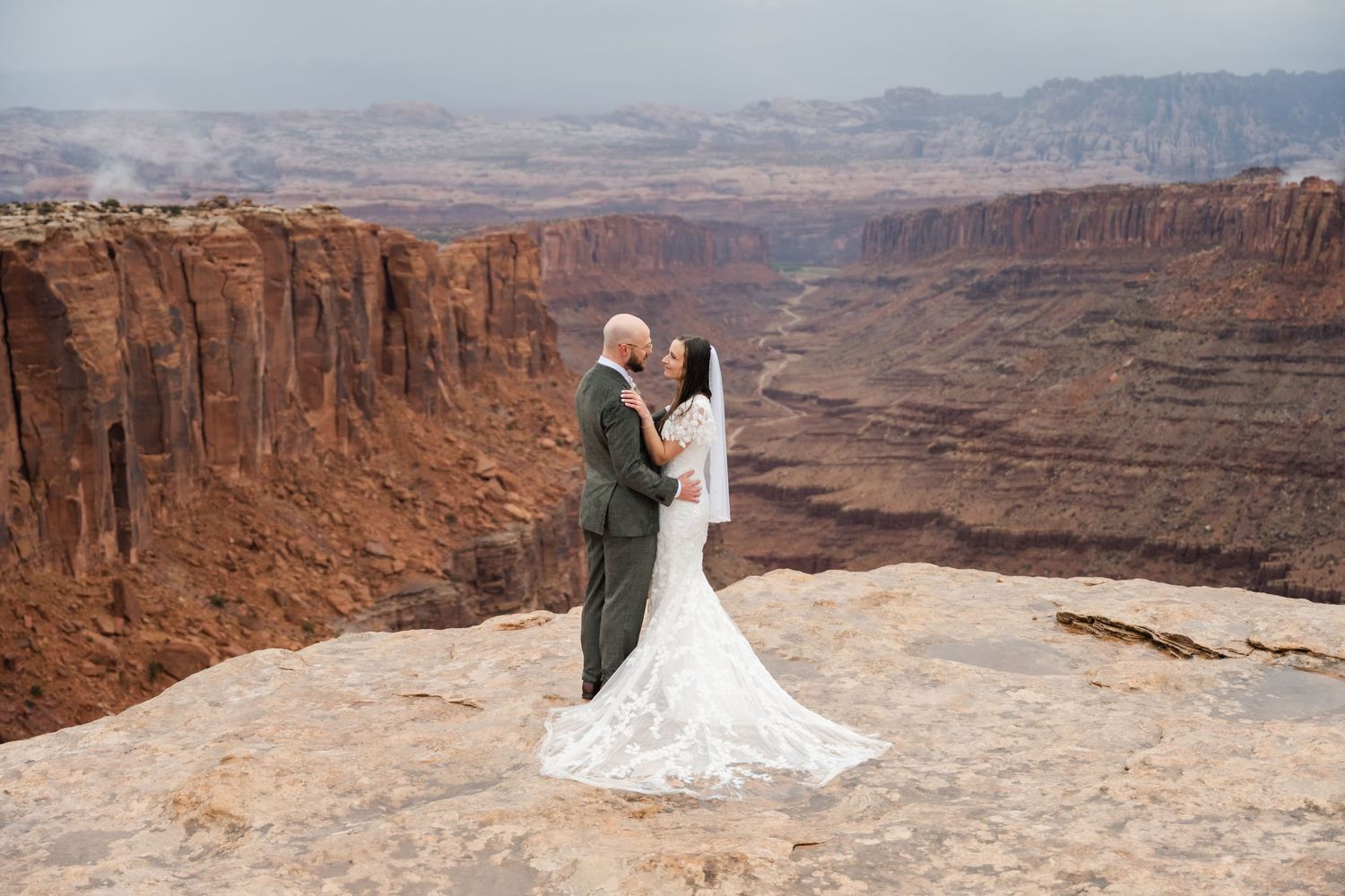 A wedding couple shares romantic moments on a cliff edge with vast canyon views. Moab elopement photographer.