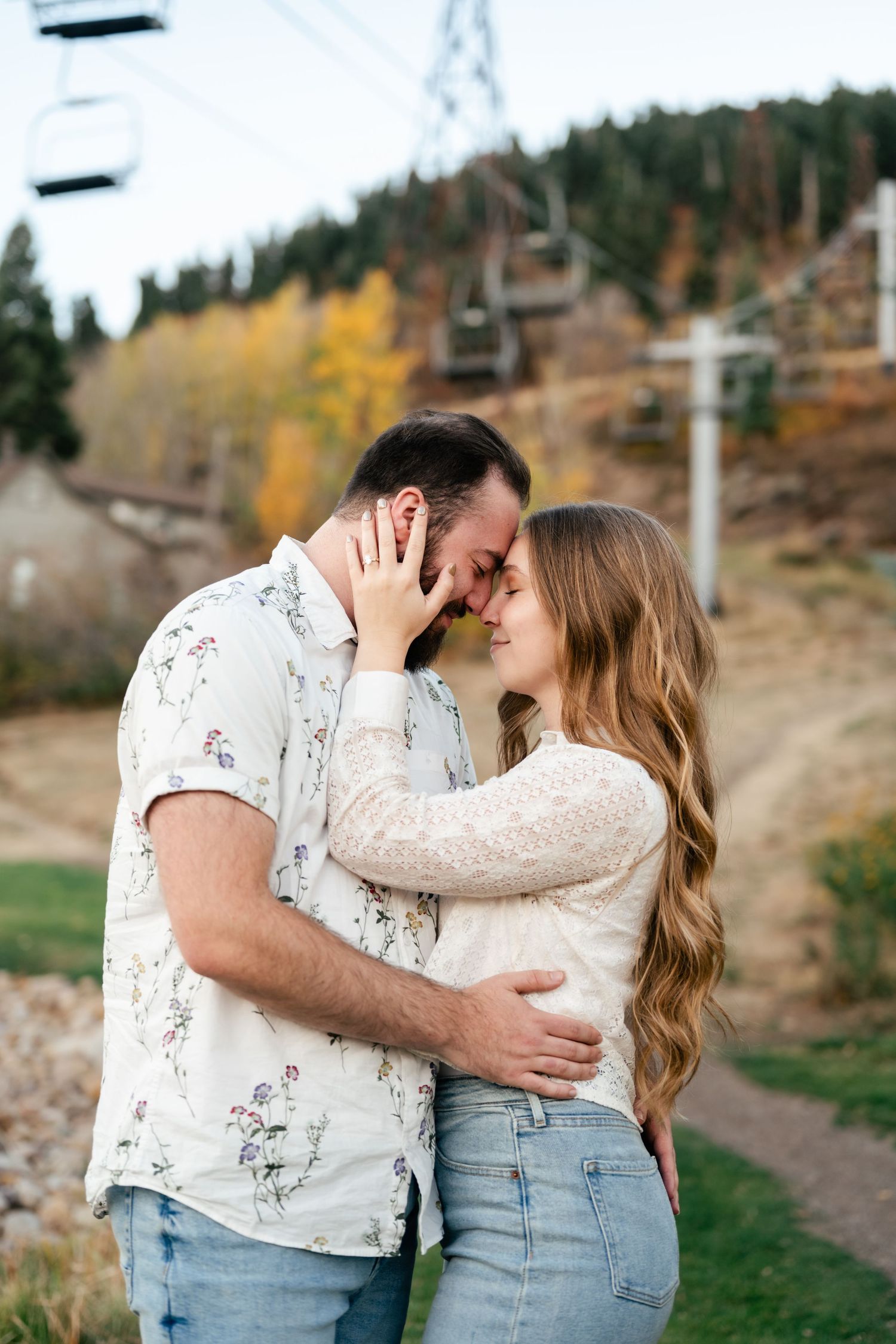 A romantic couple shares tender moments in a scenic outdoor setting with autumn foliage in the background. Engagement Photographer.